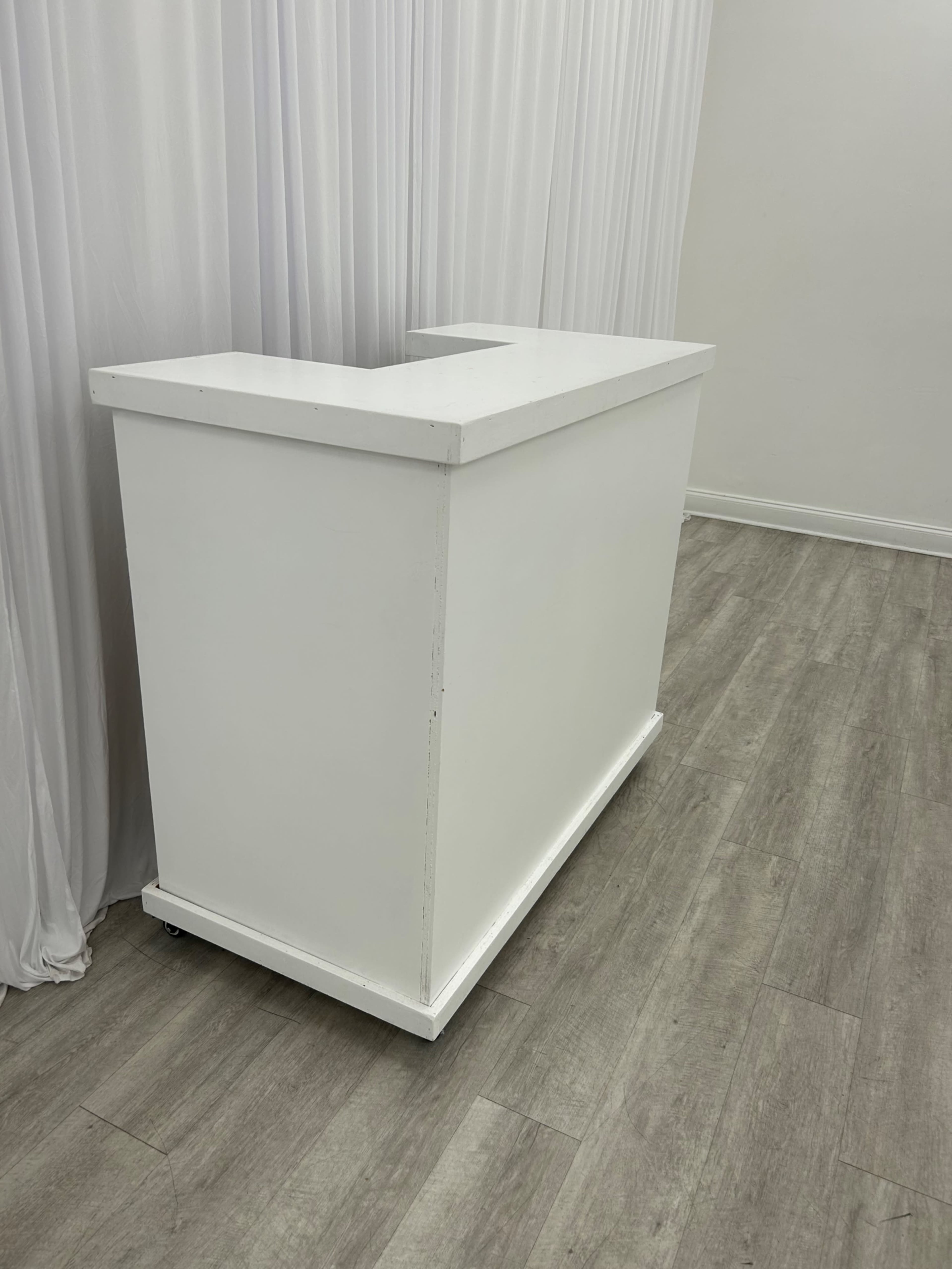 The image shows a white, rectangular reception desk with a U-shaped design, positioned against a neutral backdrop.