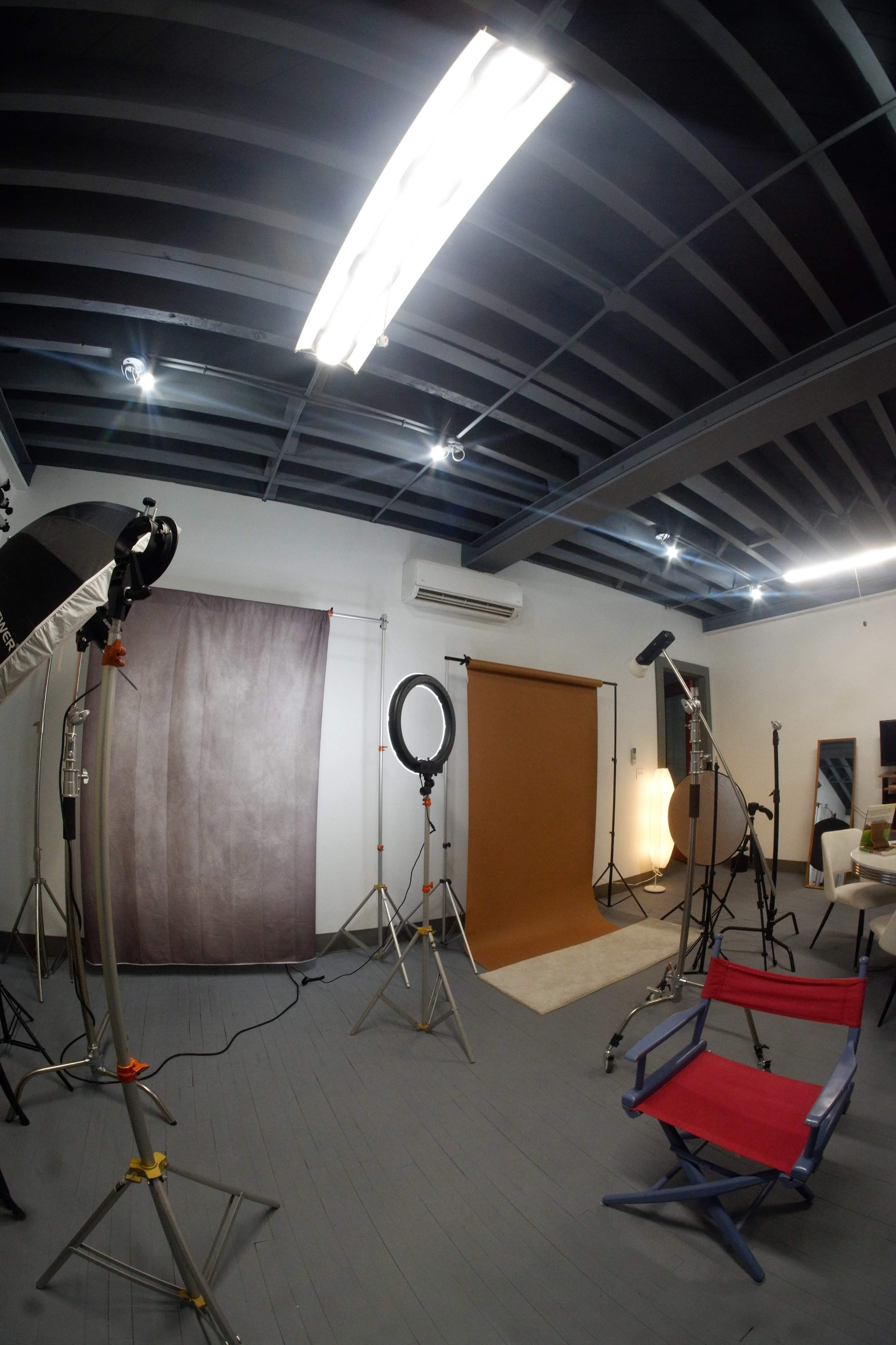 The image shows a photography studio with various backdrops, lighting equipment, and a red director's chair.