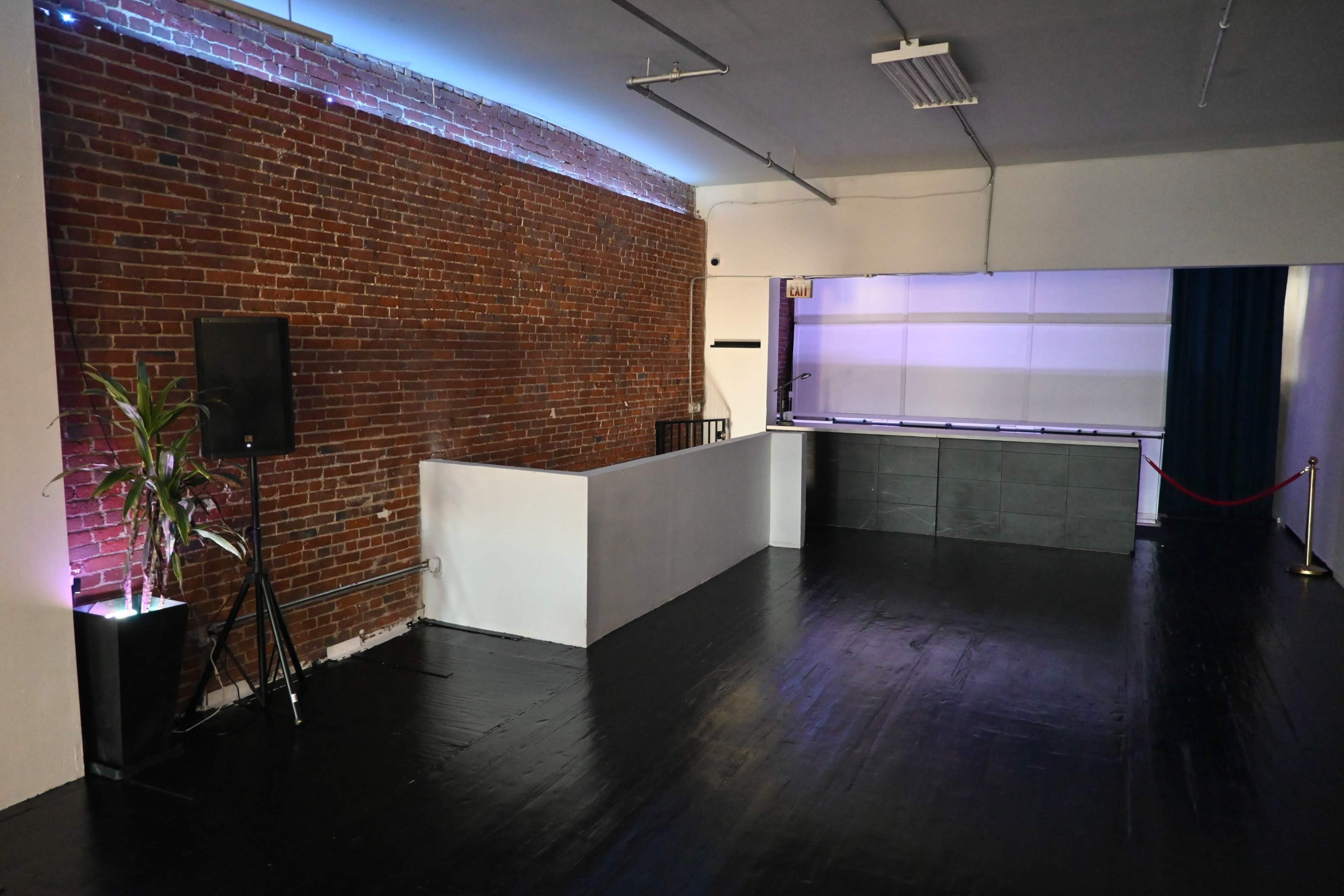 An interior space featuring a brick wall, a low counter, and a bar area with a purple backdrop and a shiny black floor.