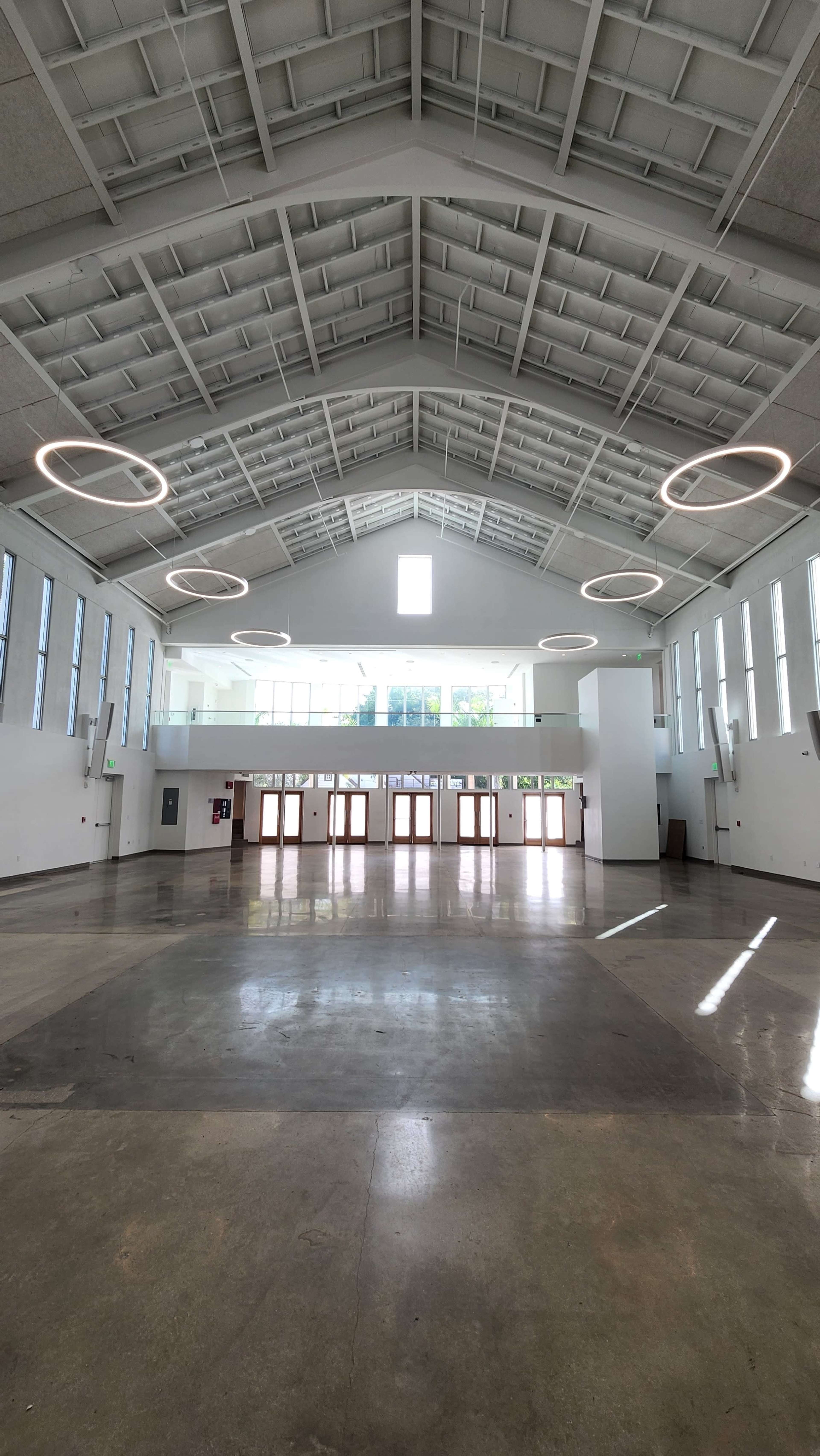 The image shows a spacious, well-lit interior of a building with high ceilings, modern lighting fixtures, and large windows.