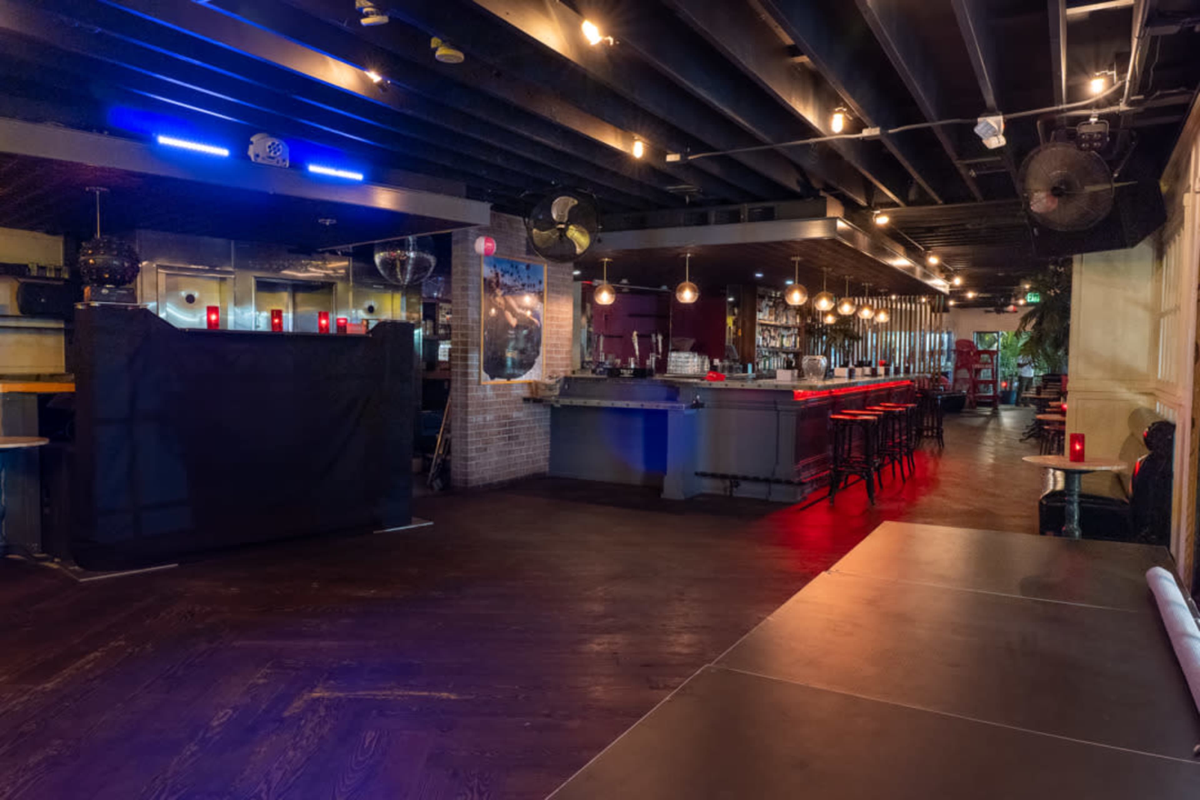 The image shows a modern bar interior with a long countertop, bar stools, and a dimly lit atmosphere.