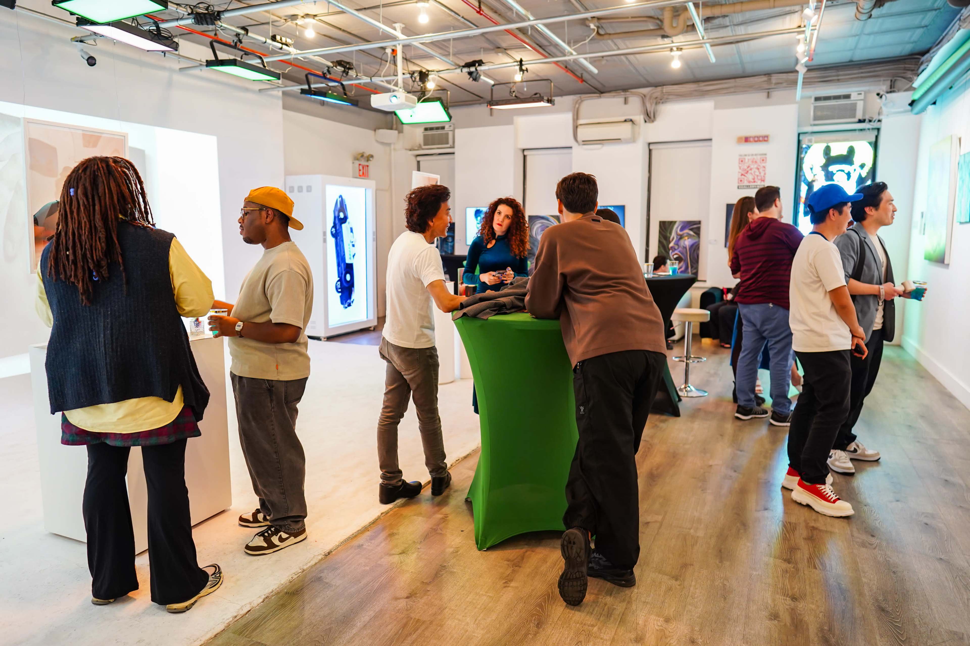 A group of people socialize and engage with displays in a modern art gallery setting.