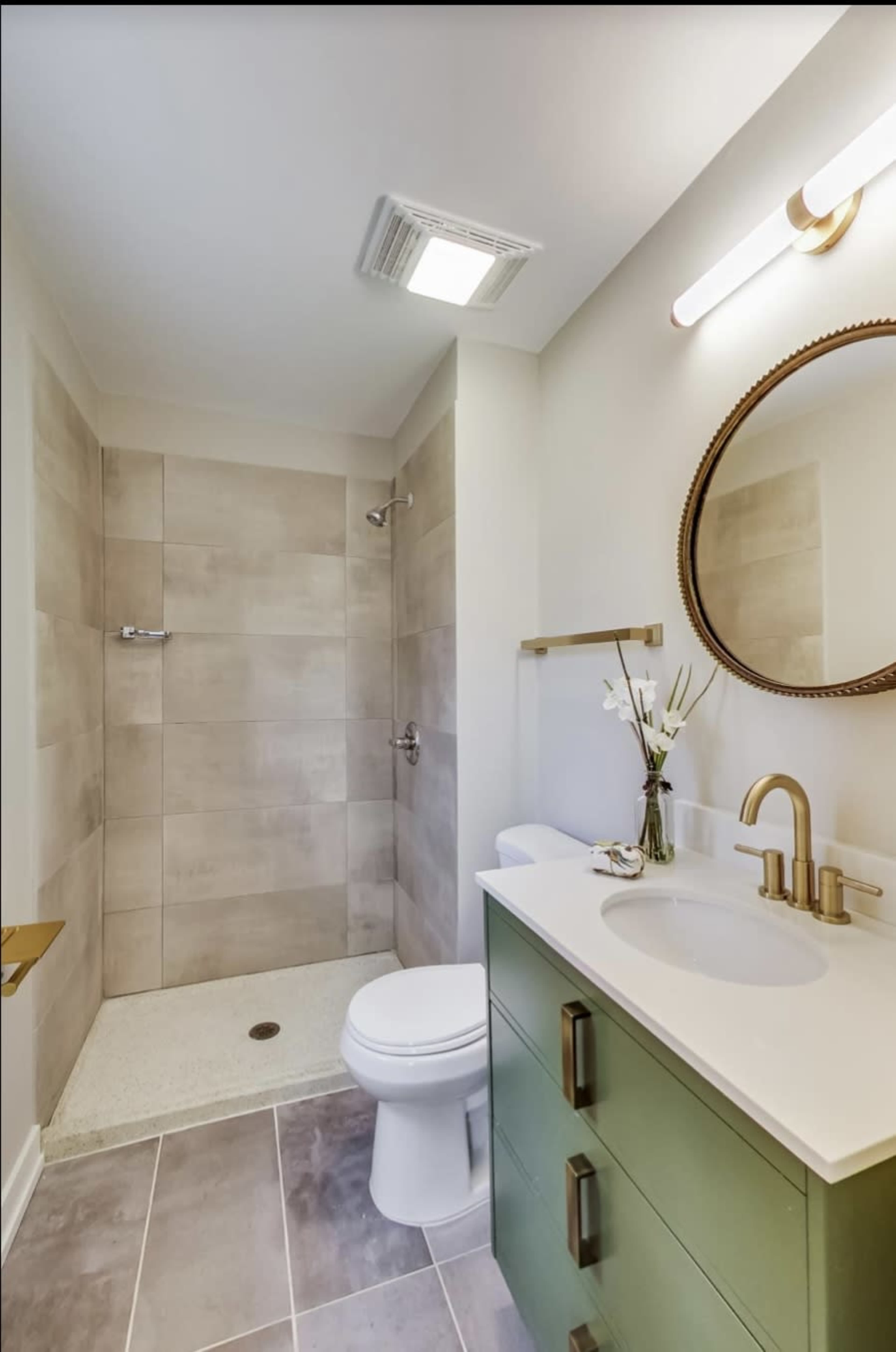 A modern bathroom featuring a shower area, a round mirror above a sink, and a green vanity with a countertop.