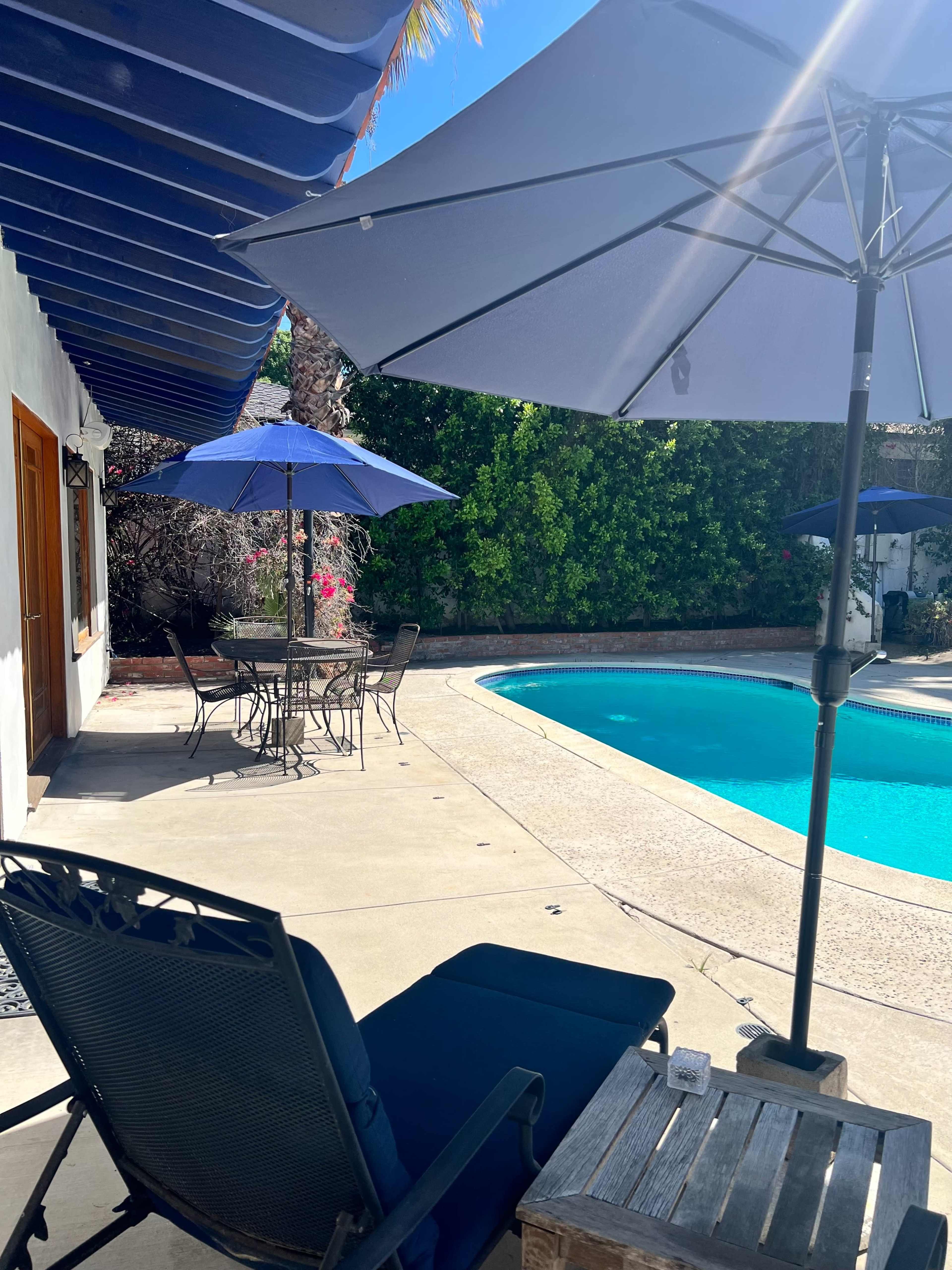 A backyard scene features a swimming pool surrounded by patio furniture, including umbrellas and a lounge chair.