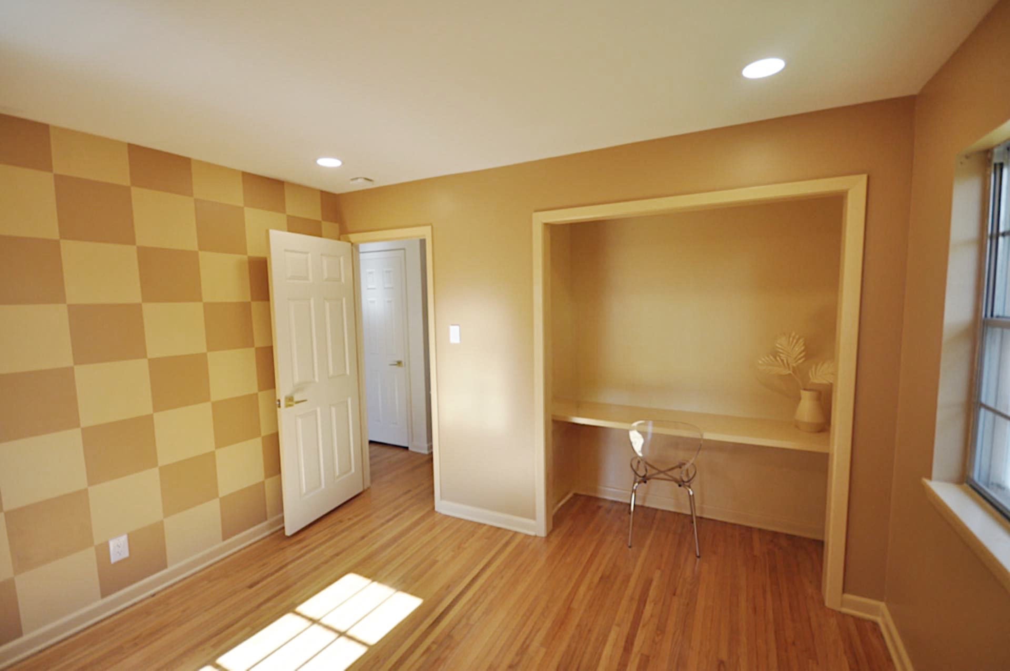 An empty room with a checkered wall design, a door leading to another space, and a built-in nook with a transparent chair.