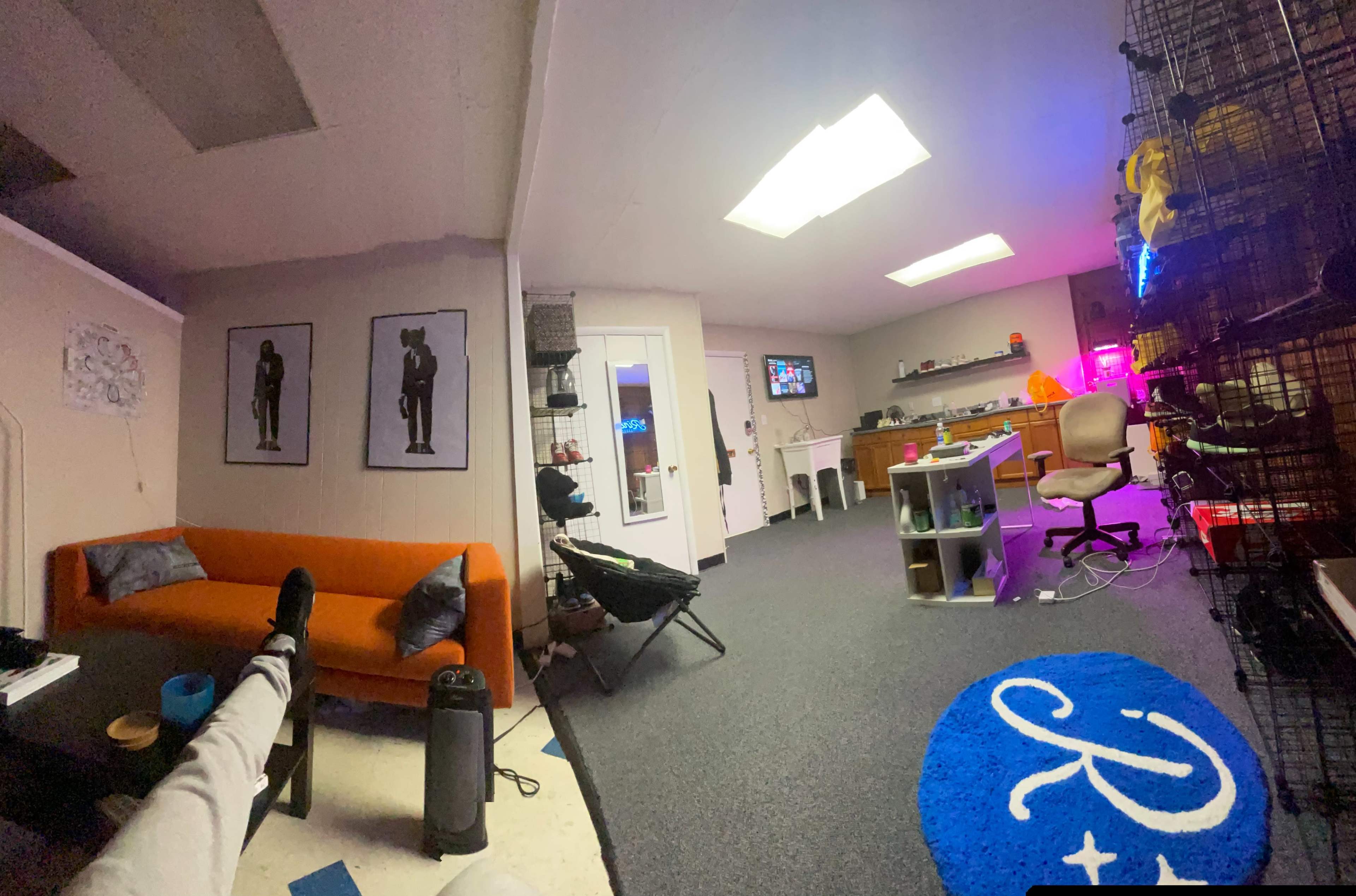 The image shows an office space with an orange couch, a desk equipped with a computer, and various items displayed on the walls and shelves.