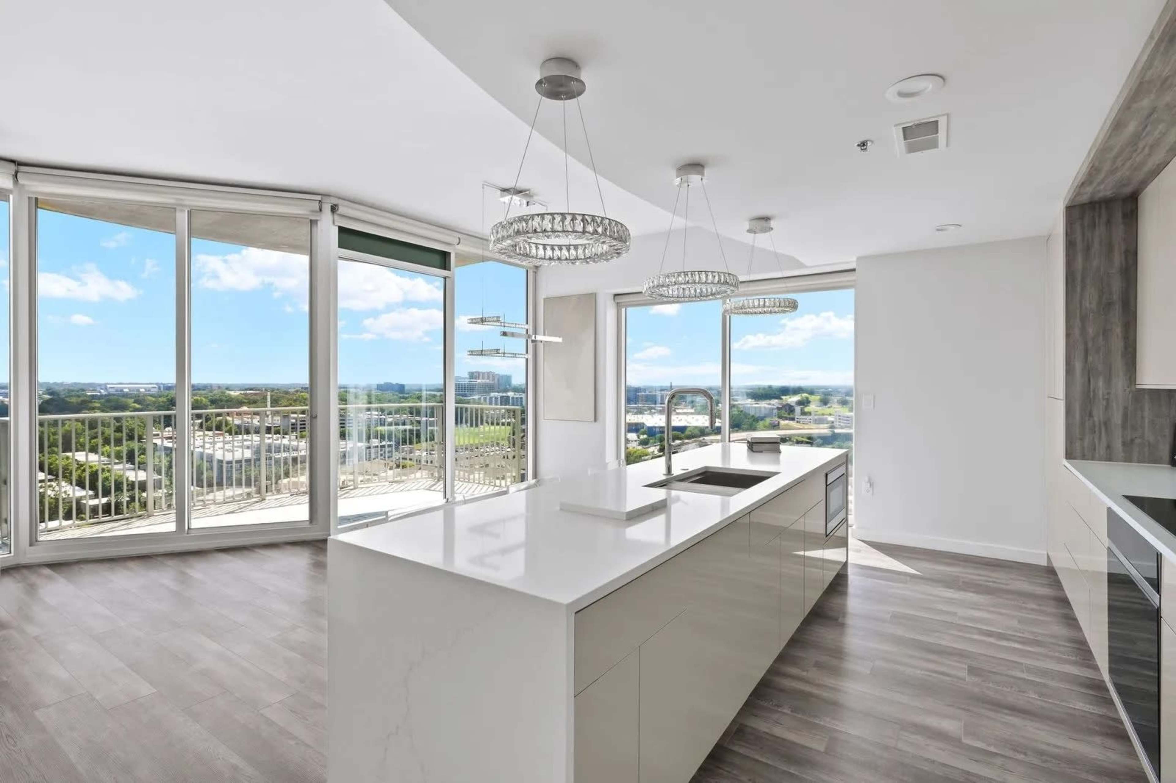 A modern kitchen features a large island and floor-to-ceiling windows with a view of the city.