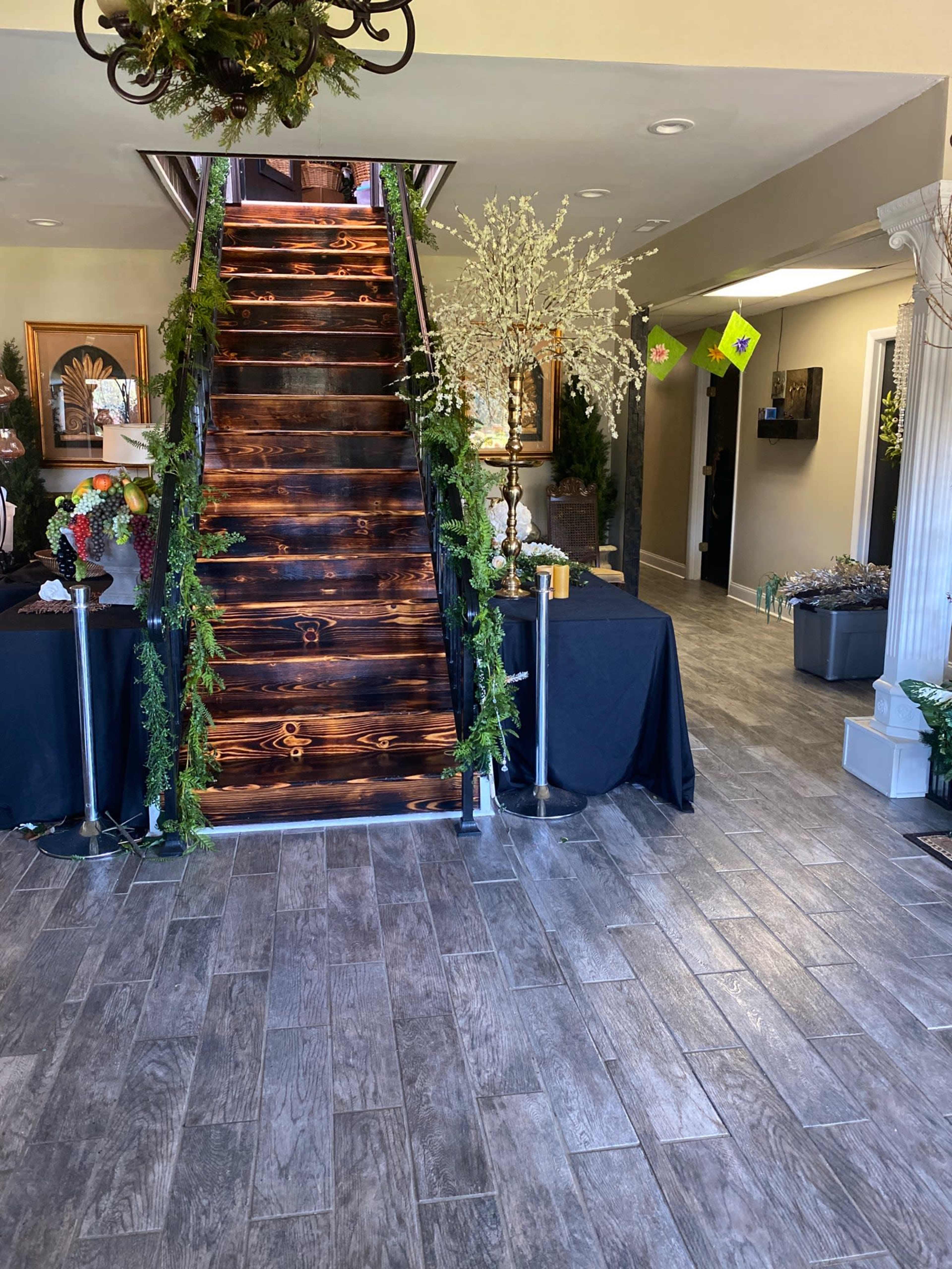A wooden staircase with greenery decor leading up, situated in a room with a tiled floor and various decorative items.