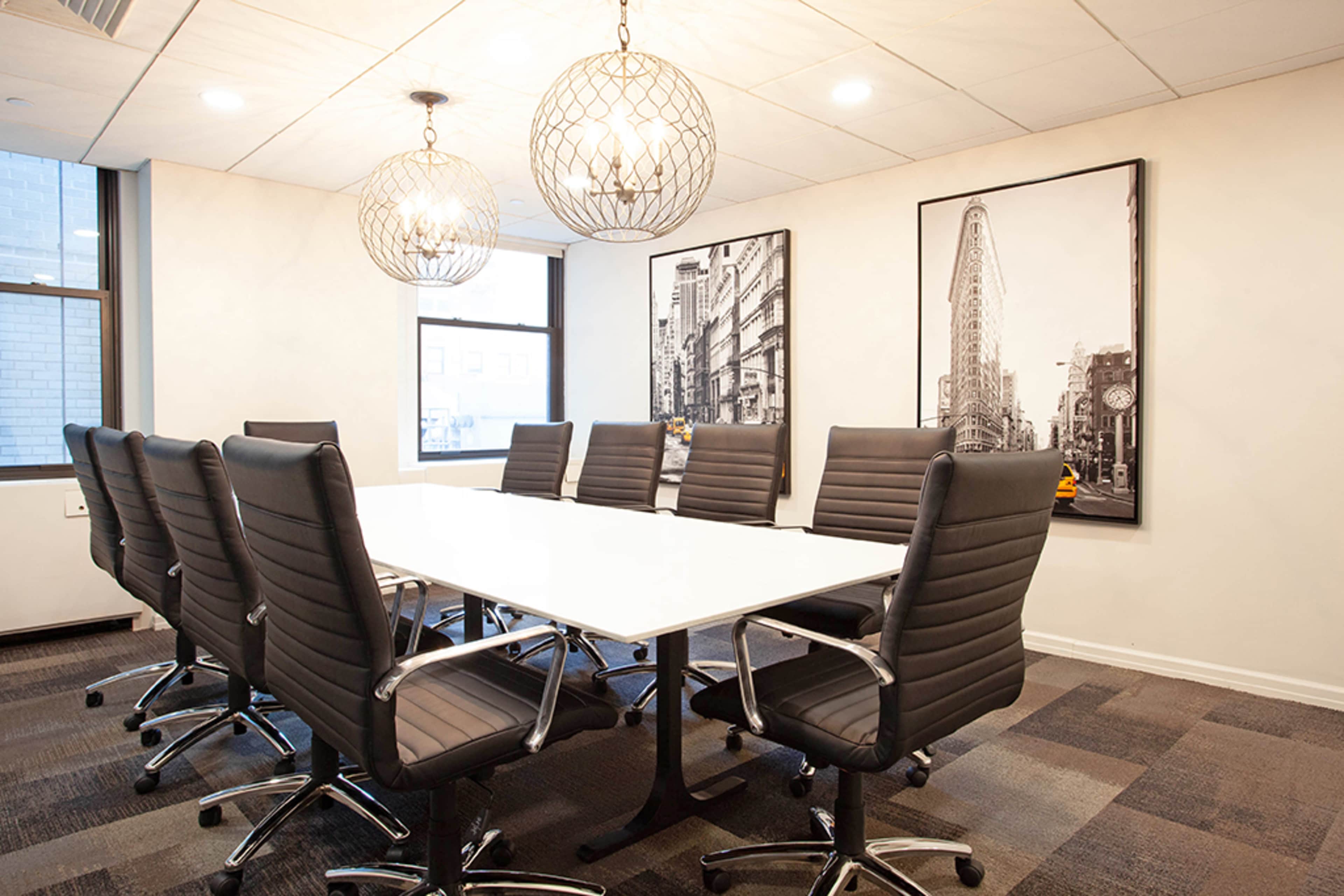 A modern conference room features a long white table surrounded by eight black chairs, with large windows and artistic wall decor.