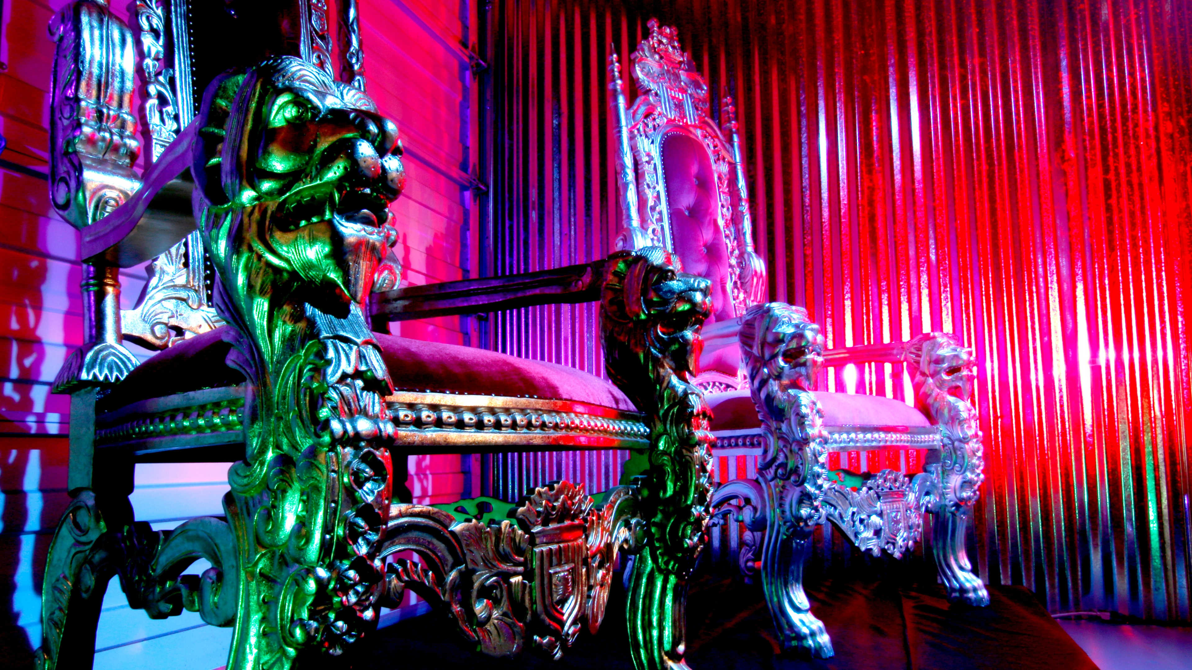 Two ornate throne chairs with lion motifs set against a brightly lit, colorful backdrop.