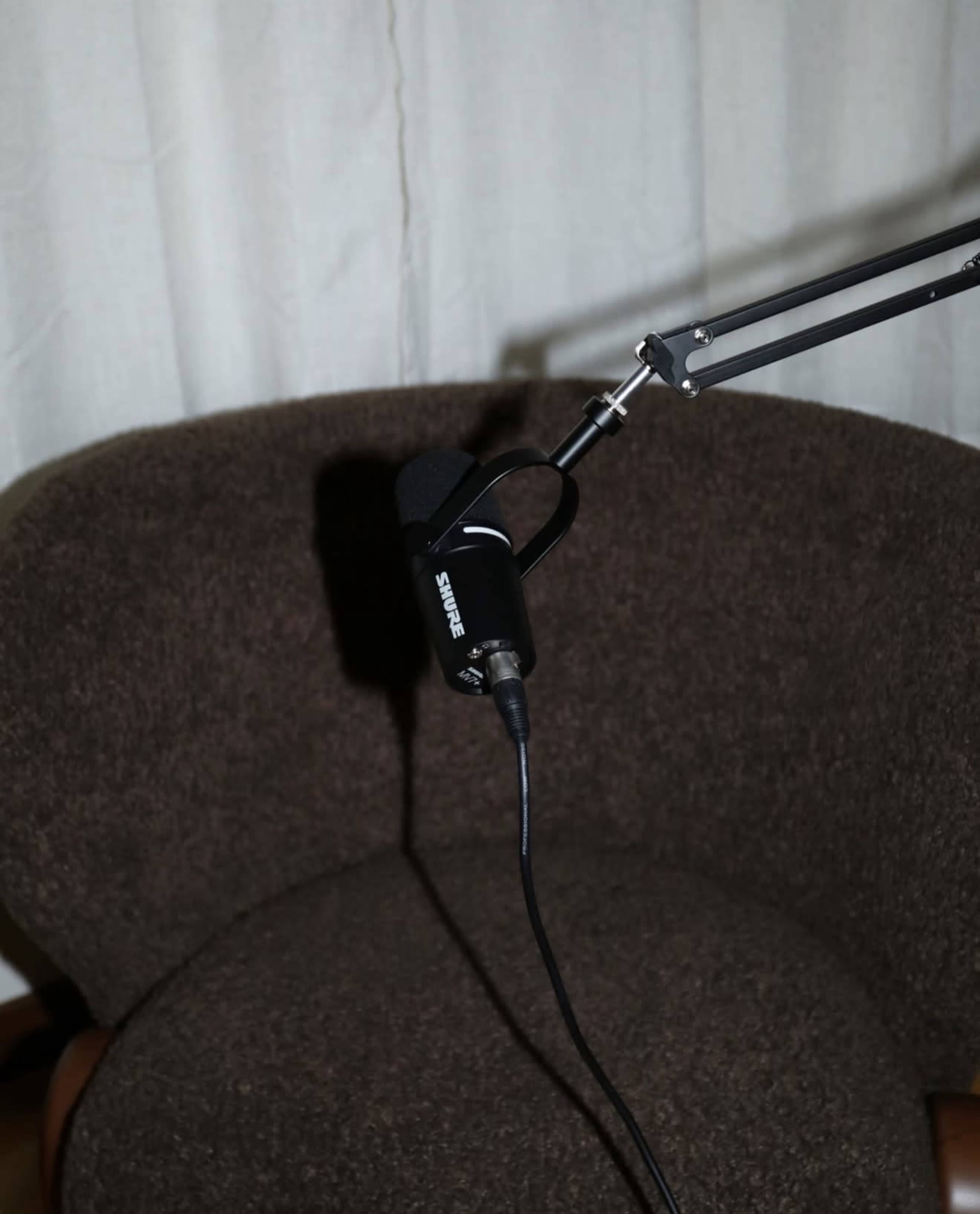 A microphone is mounted on an adjustable arm positioned over a brown upholstered chair.