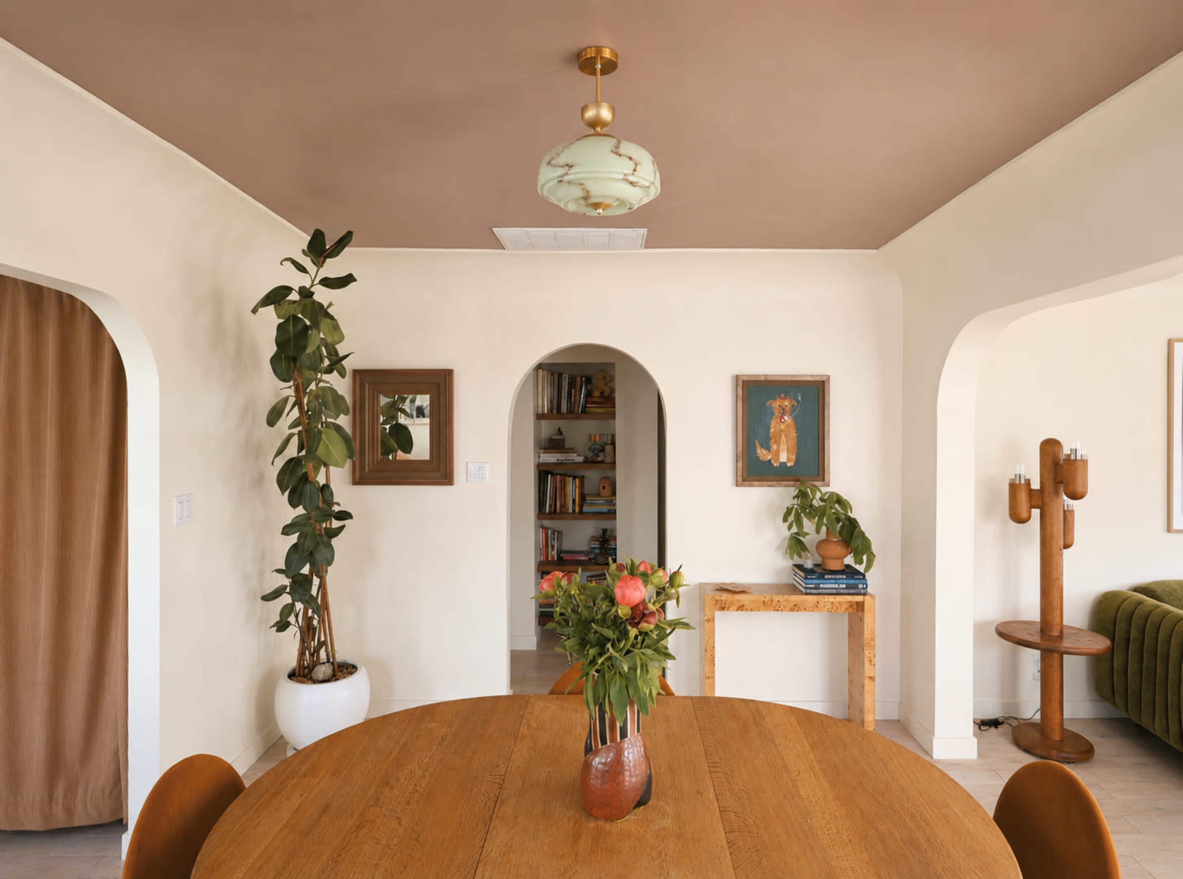 The image shows a well-decorated dining area featuring a round wooden table, a vase of flowers, and archways leading to other rooms.