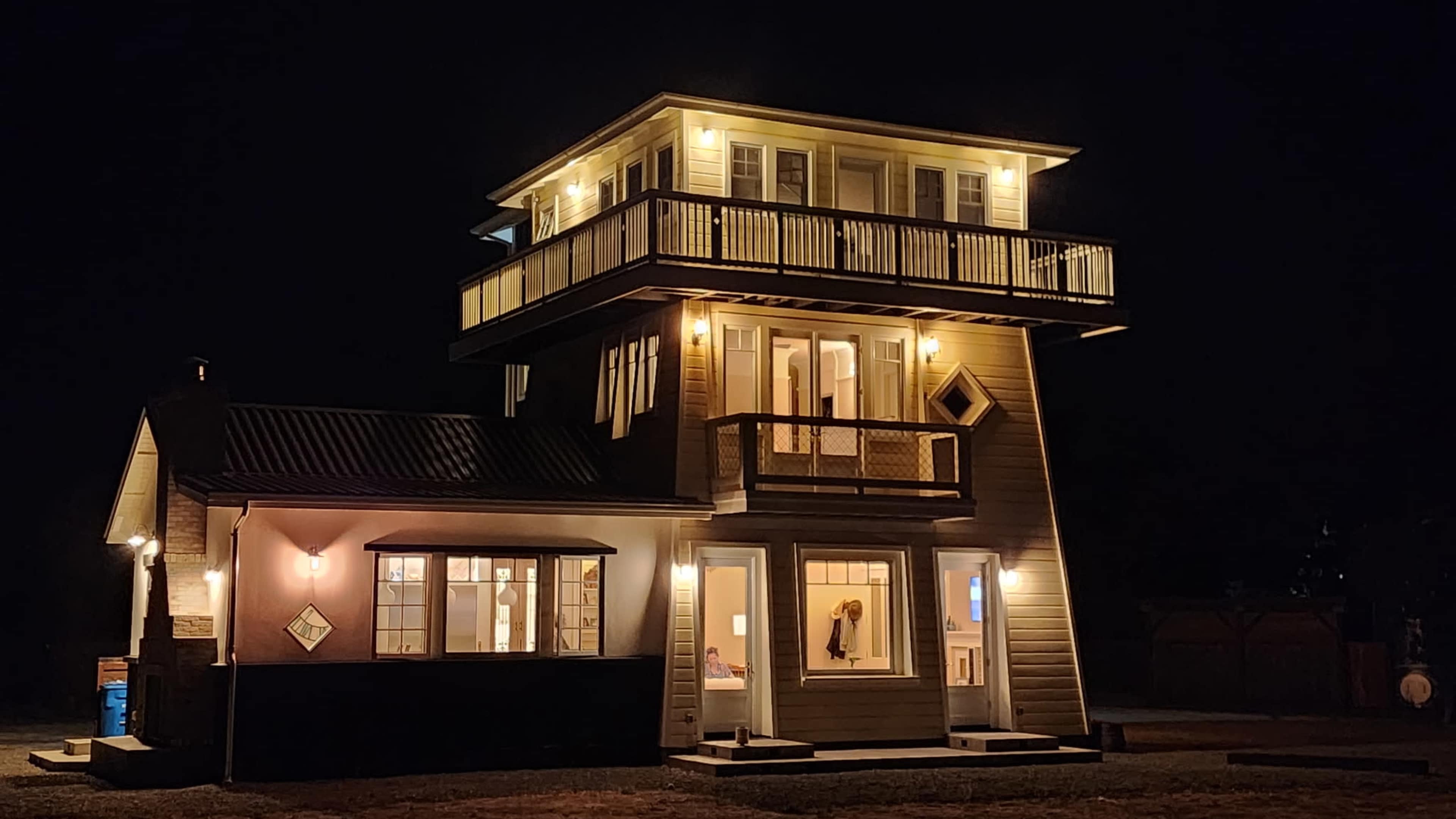 A multi-story house with a striking architectural design is illuminated at night, featuring balconies and large windows.