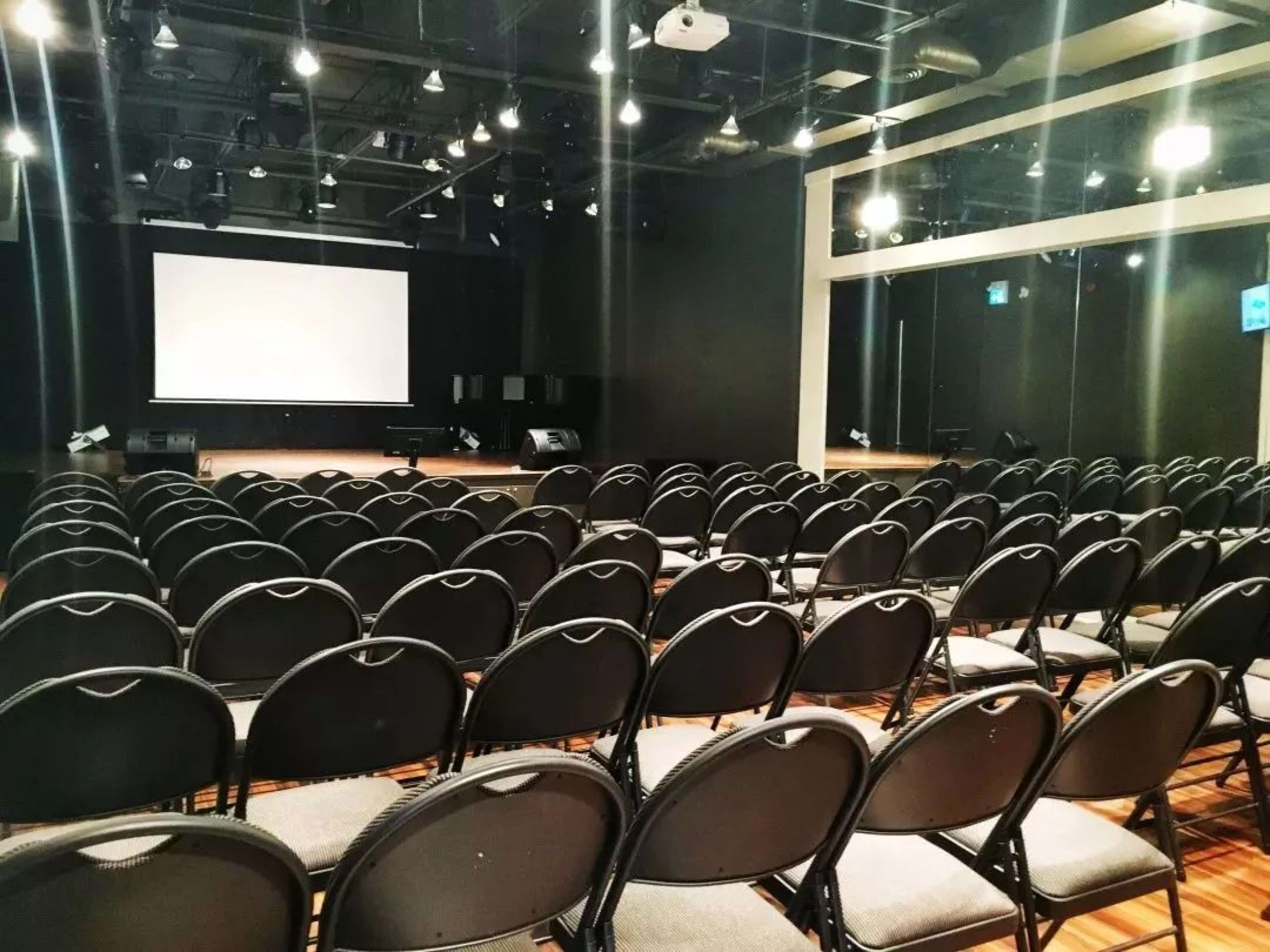 A large auditorium with rows of black chairs facing a blank projection screen at the front.