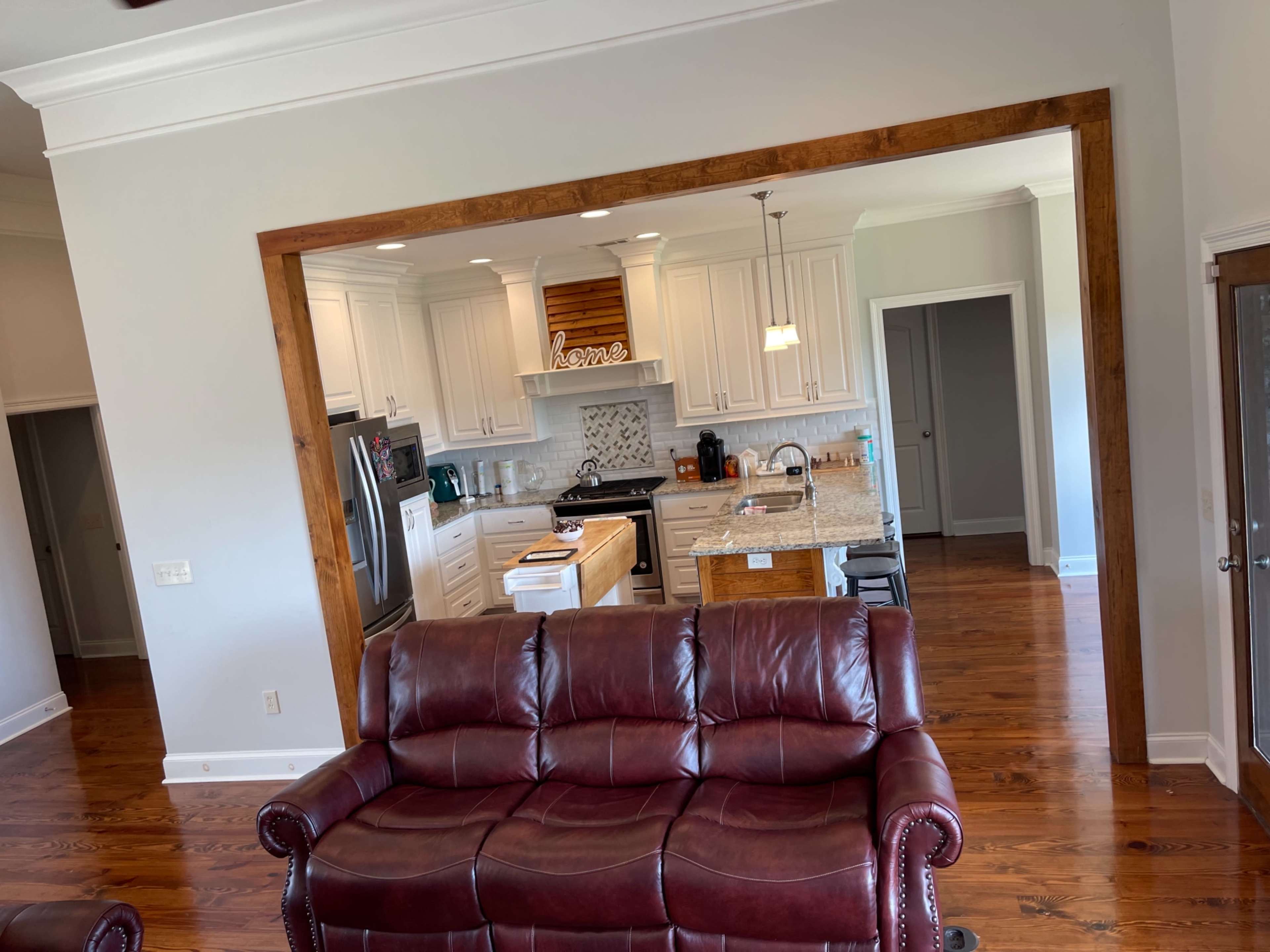 A living room with a brown leather sofa facing an open kitchen area featuring white cabinets and a granite countertop.