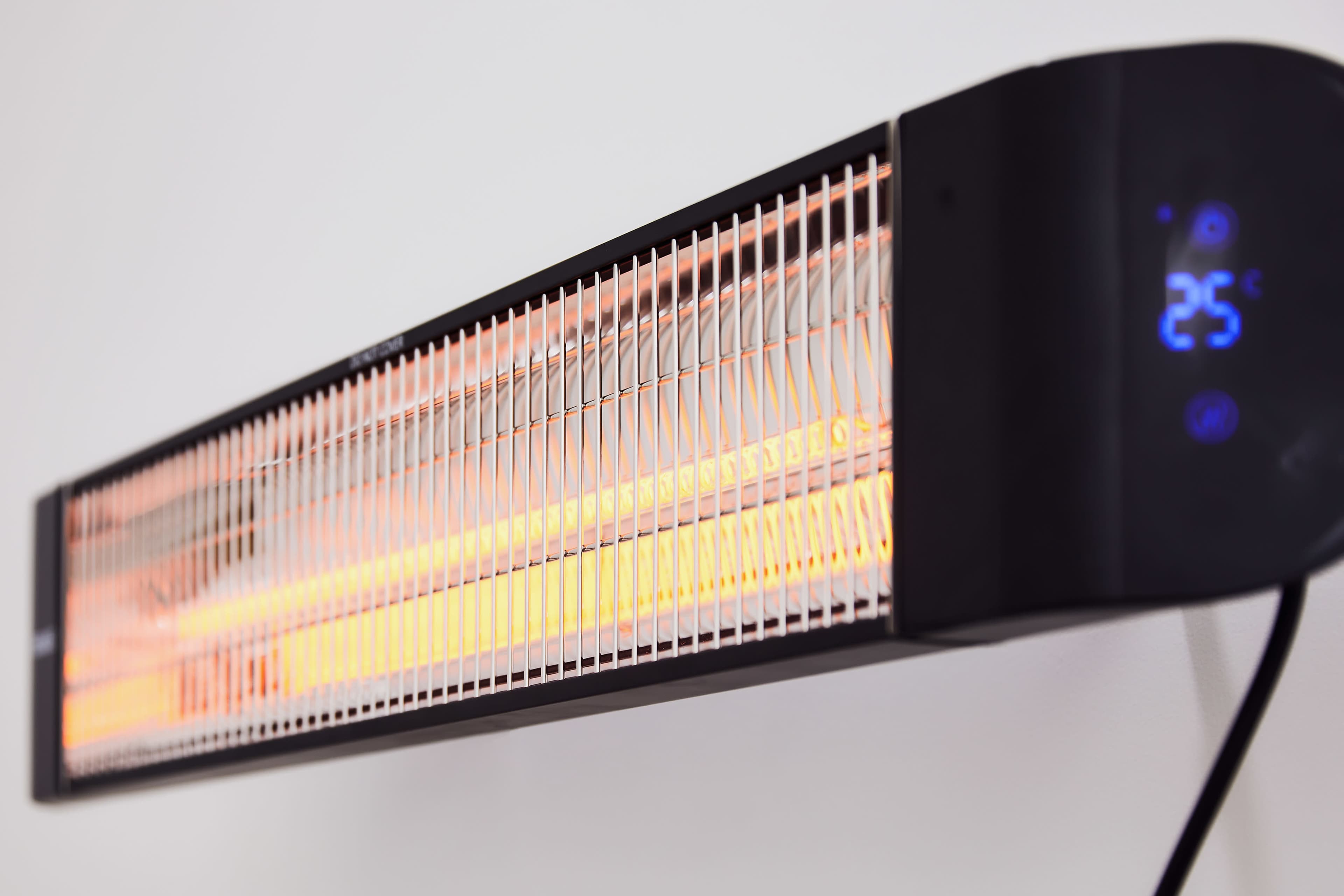 A wall-mounted electric heater emits warm light through a long, narrow heating element.