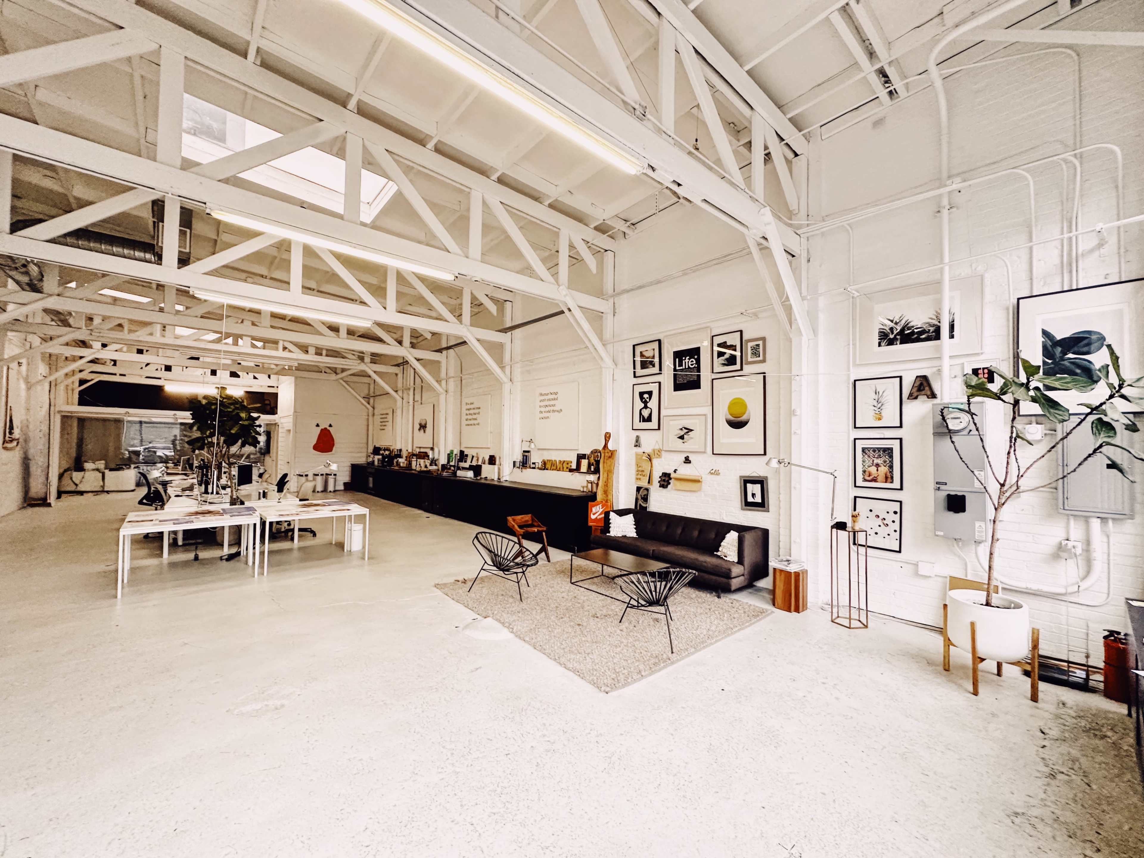 A spacious, well-lit interior of an art studio or gallery with white walls, exposed beams, and various artworks displayed on the walls.