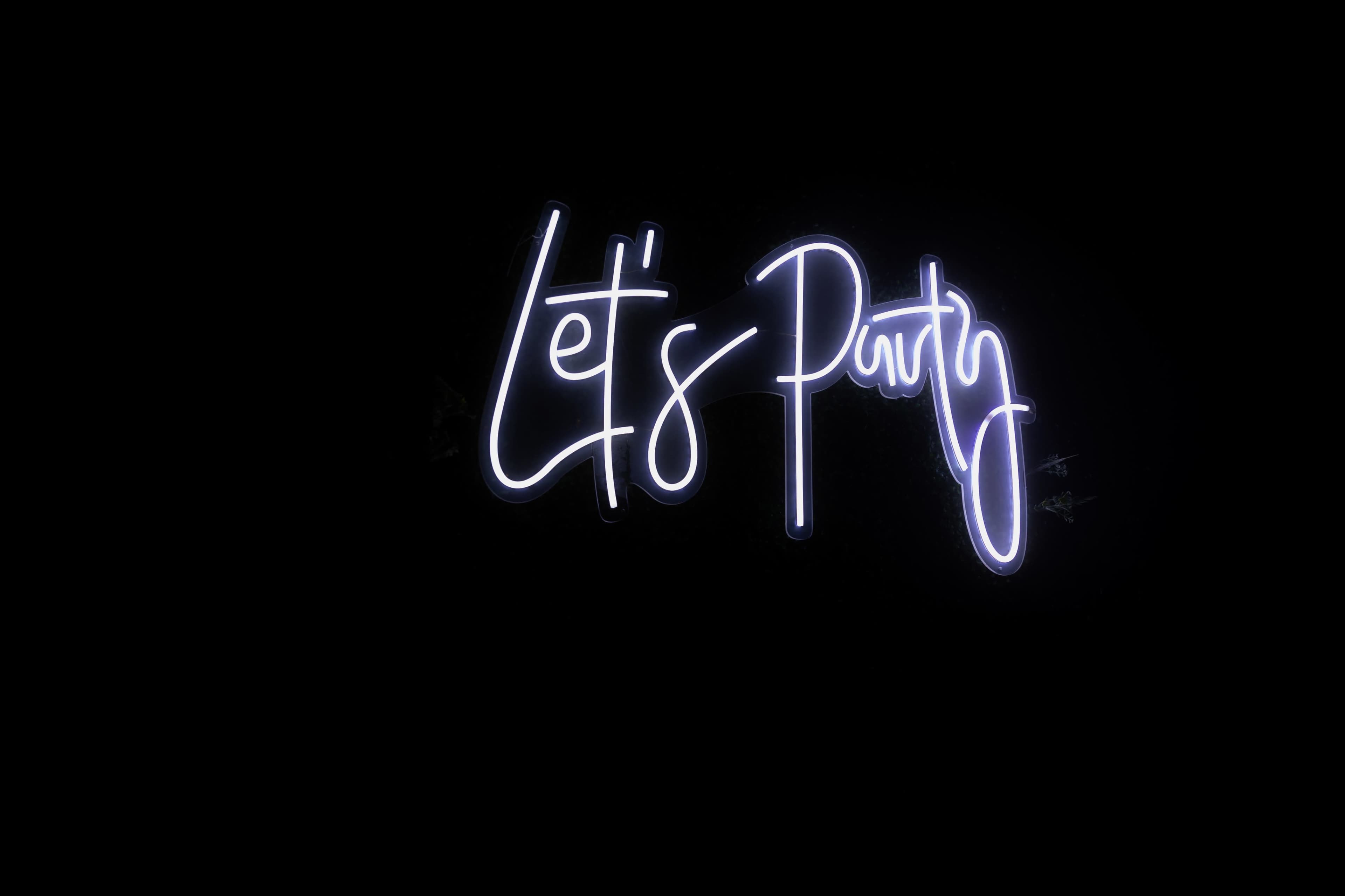 A neon sign displays the phrase "Let's Party" in bright white lettering against a black background.