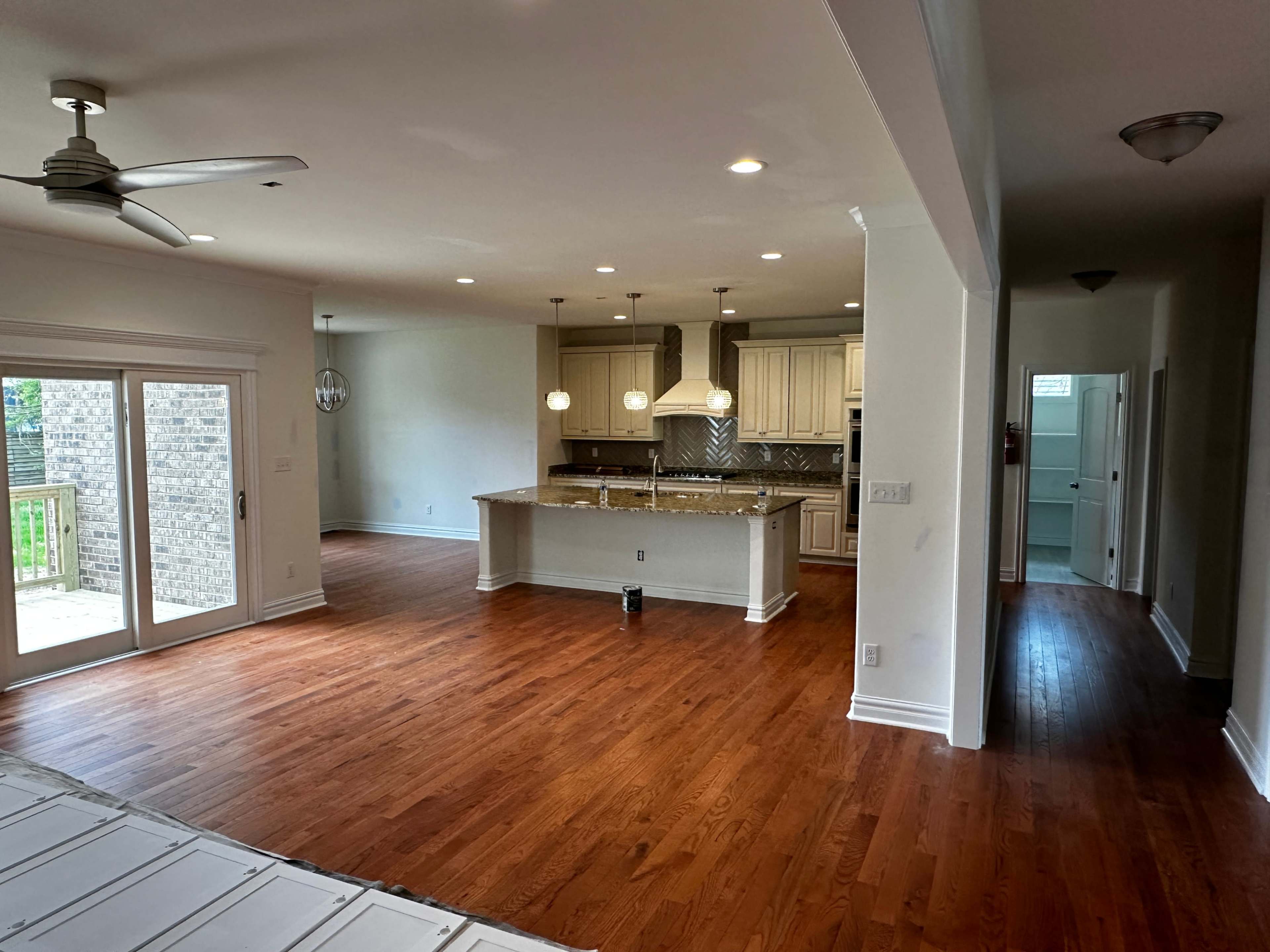 A spacious living area with hardwood floors, a kitchen featuring an island with pendant lights, and a sliding door leading to an outdoor deck.
