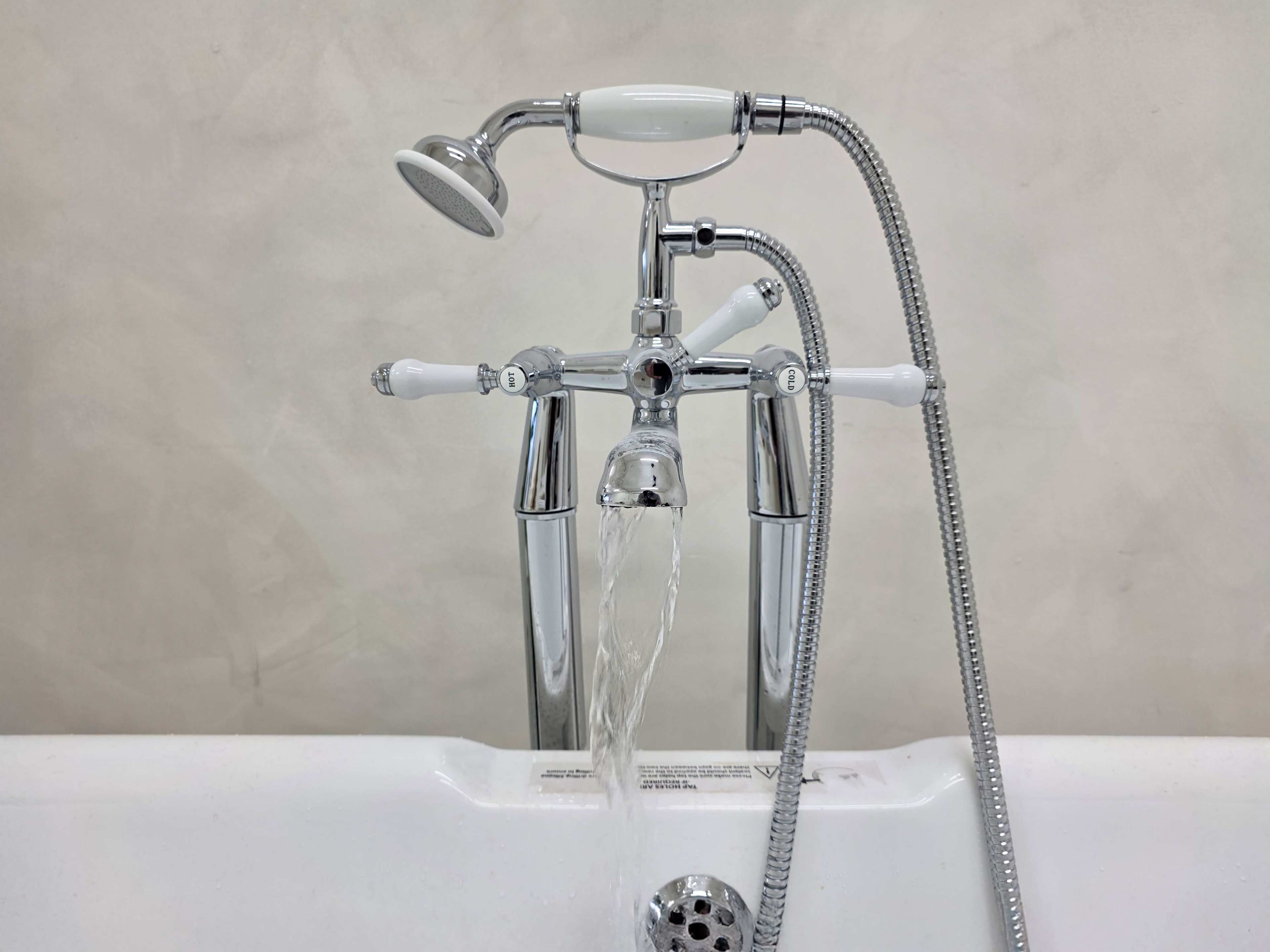 A chrome bathtub faucet with a handheld showerhead is pouring water into a white bathtub.