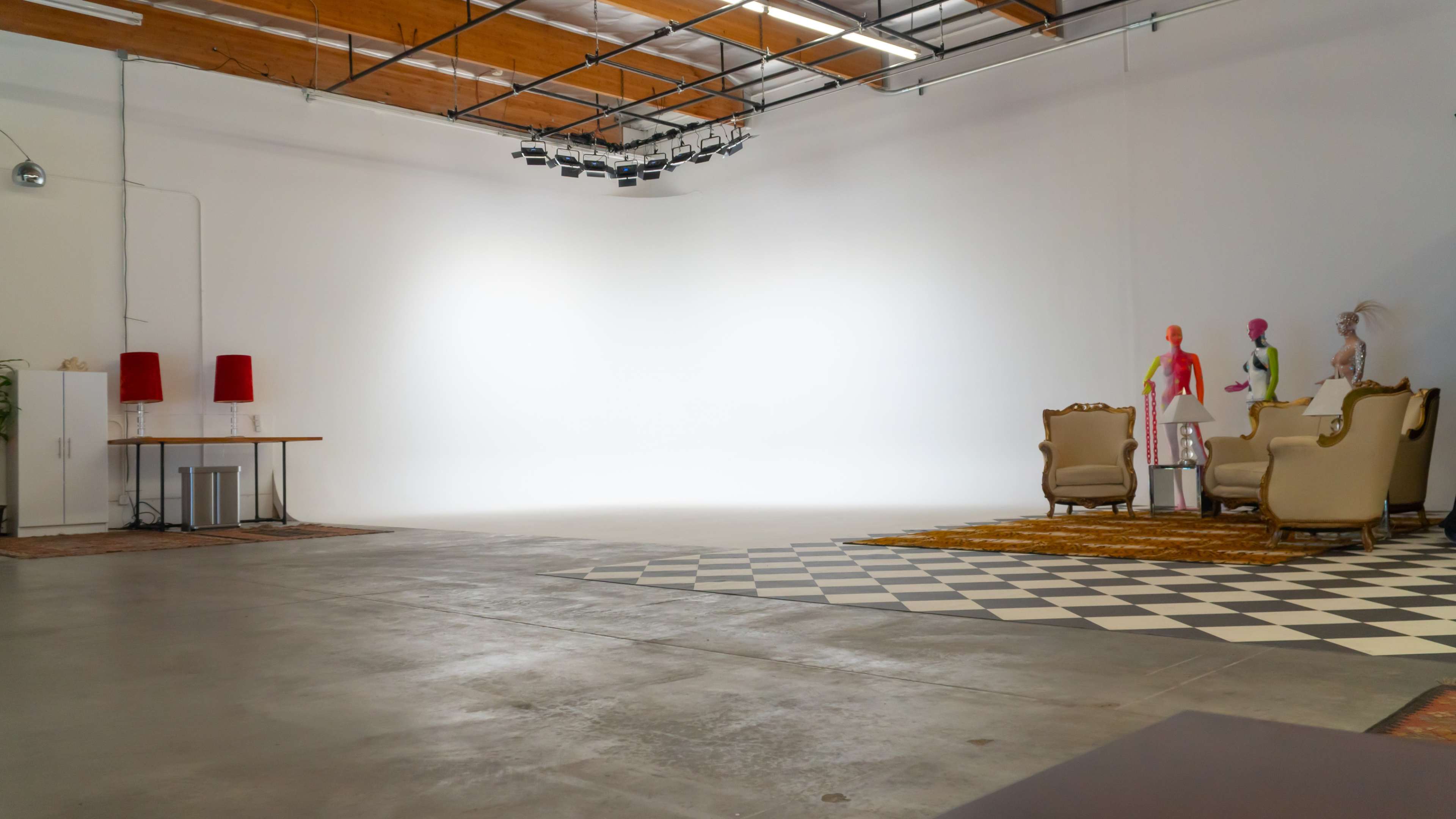 A spacious studio with a white backdrop, two armchairs, a patterned rug, a table, and several mannequins arranged in the corner.
