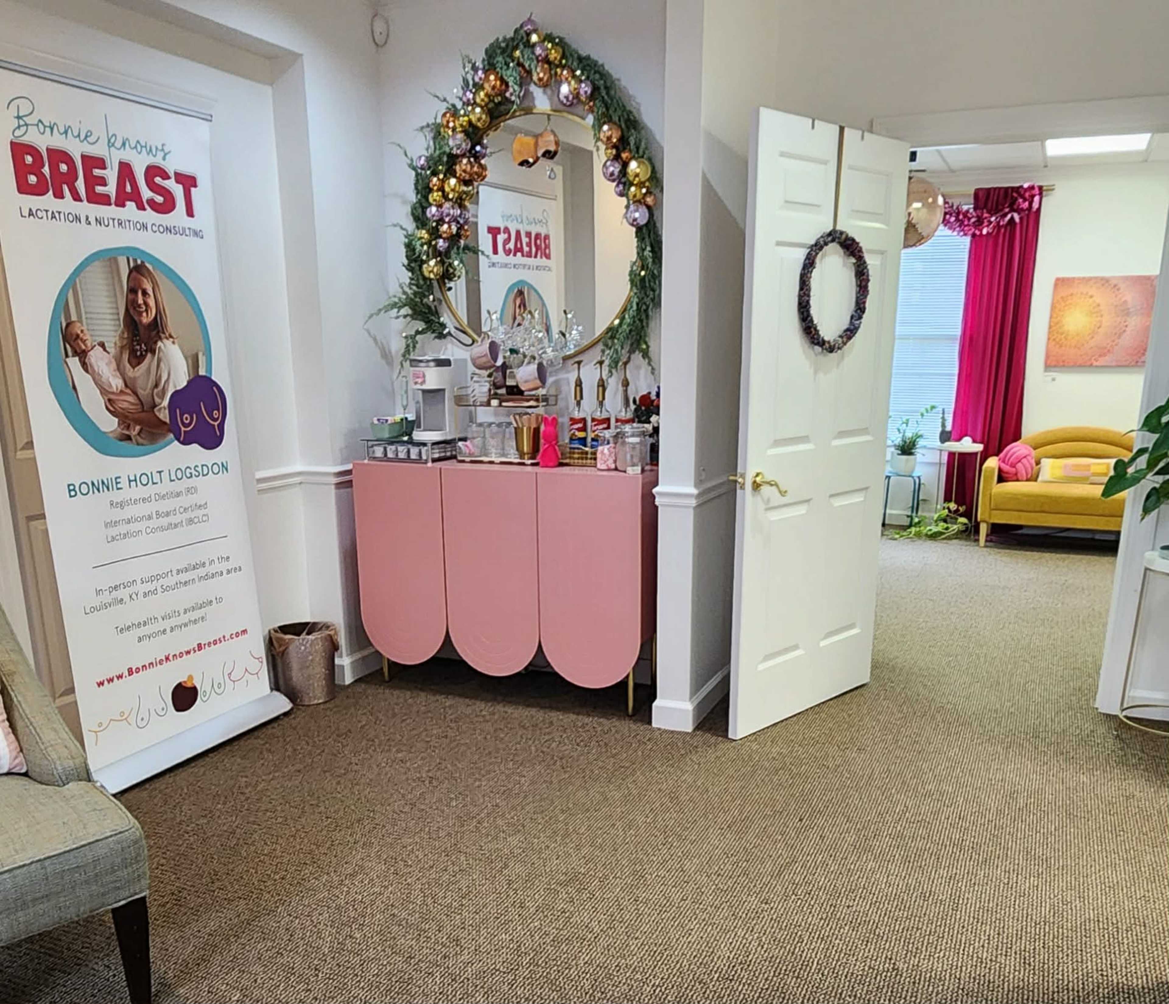 The image shows a brightly lit room featuring a pink storage cabinet, a banner about lactation consulting, and a cozy seating area with a yellow couch in the background.