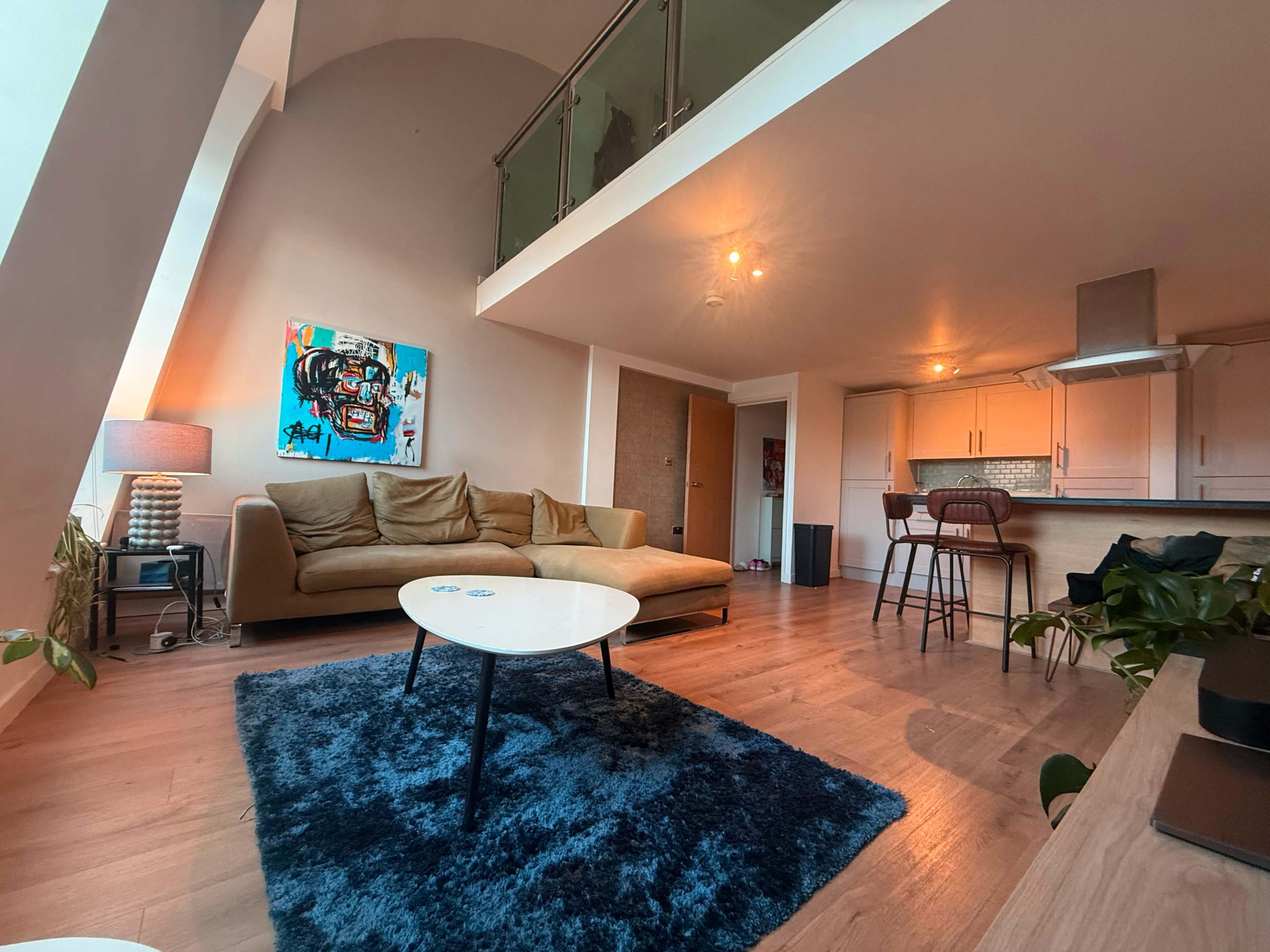 The image shows a modern living room with a large sectional couch, a coffee table, and a kitchen area visible in the background, all enhanced by natural light.