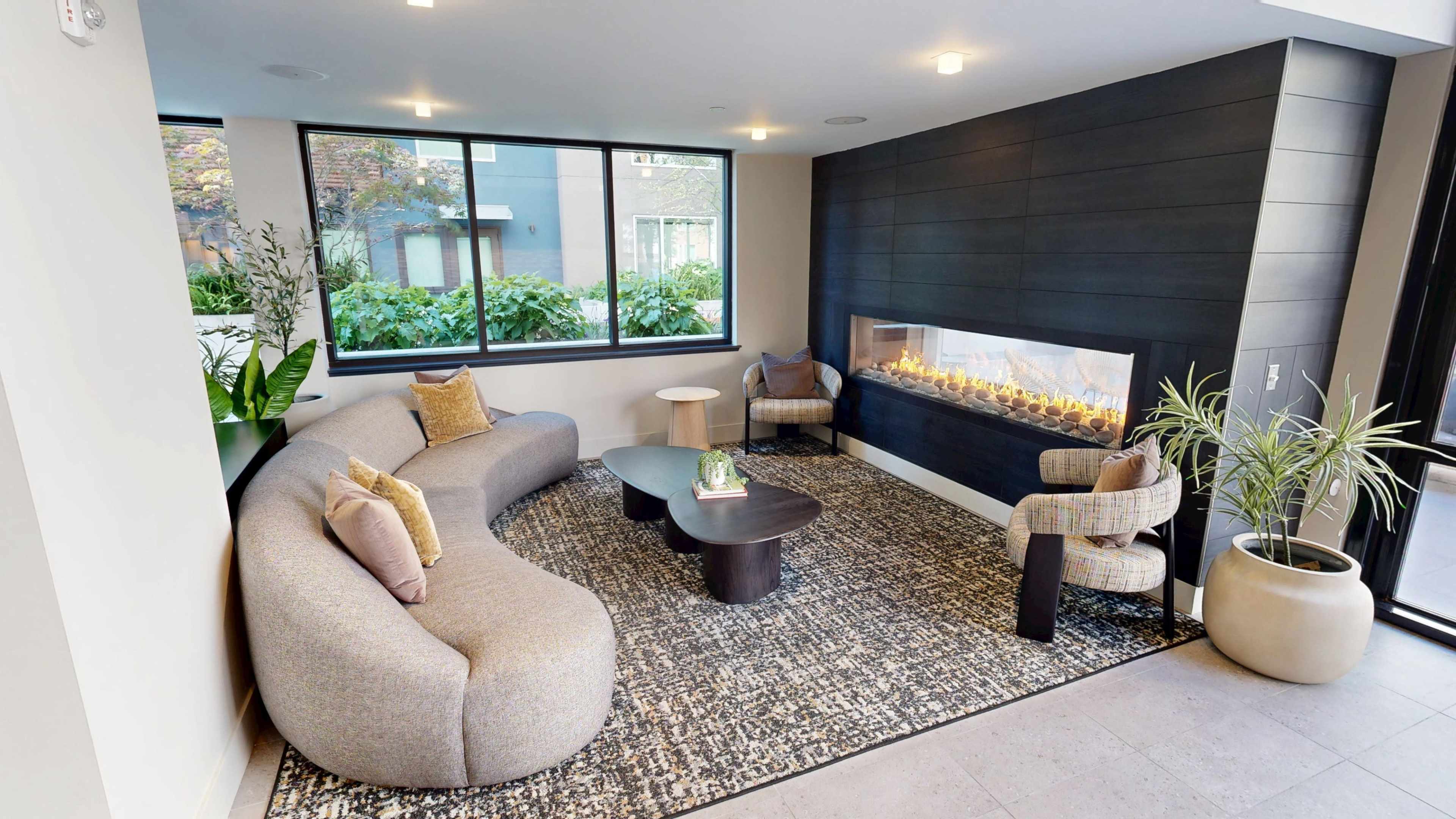A modern seating area features a curved sofa, a coffee table, and an elegant gas fireplace, all illuminated by large windows.