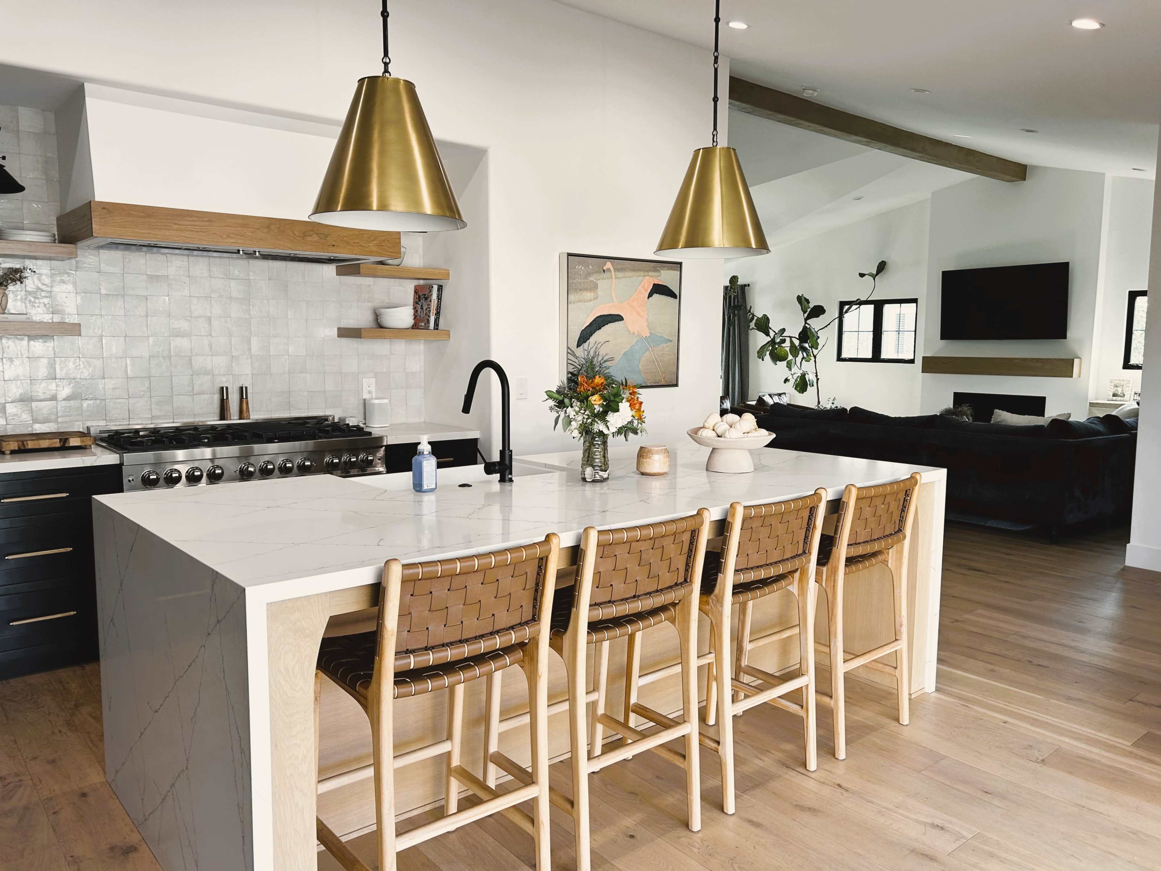 A modern kitchen features a large island with barstools, gold pendant lights, and a stainless-steel stove.