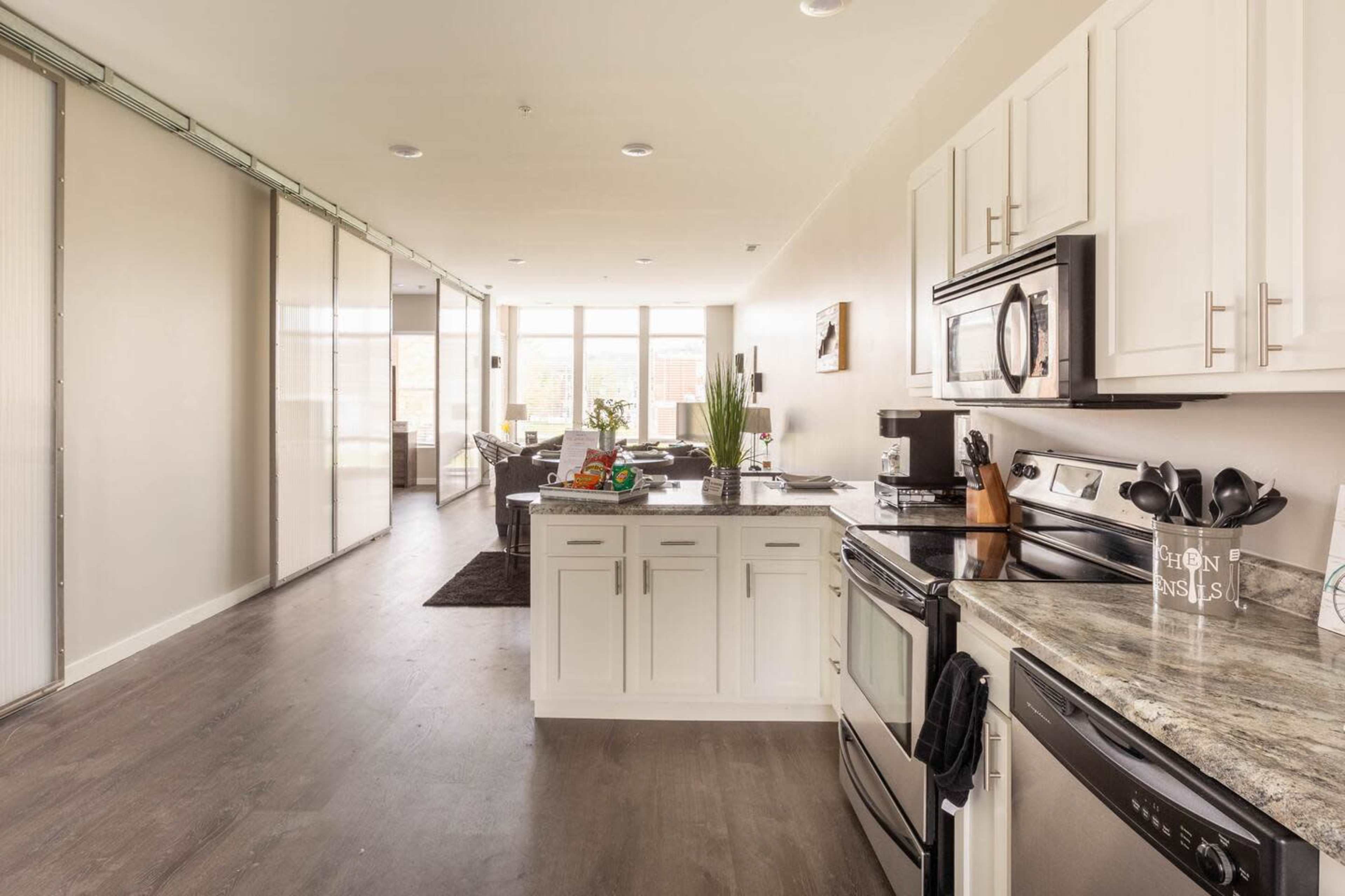 A modern kitchen with white cabinetry and stainless steel appliances, leading into an open-concept living area filled with natural light.