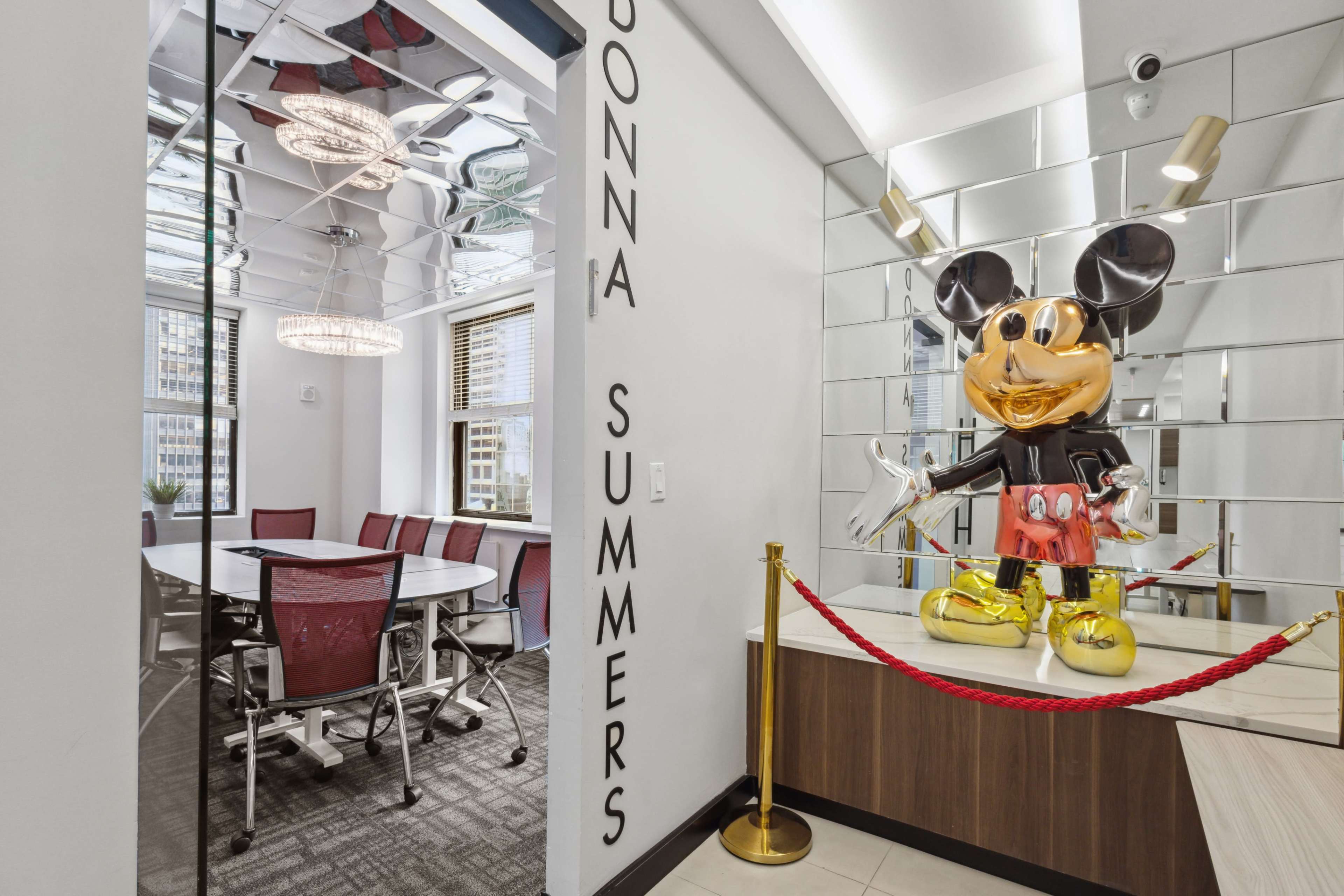 A modern conference room with a large round table and a decorative statue of Mickey Mouse in the corner, surrounded by a red rope barrier.