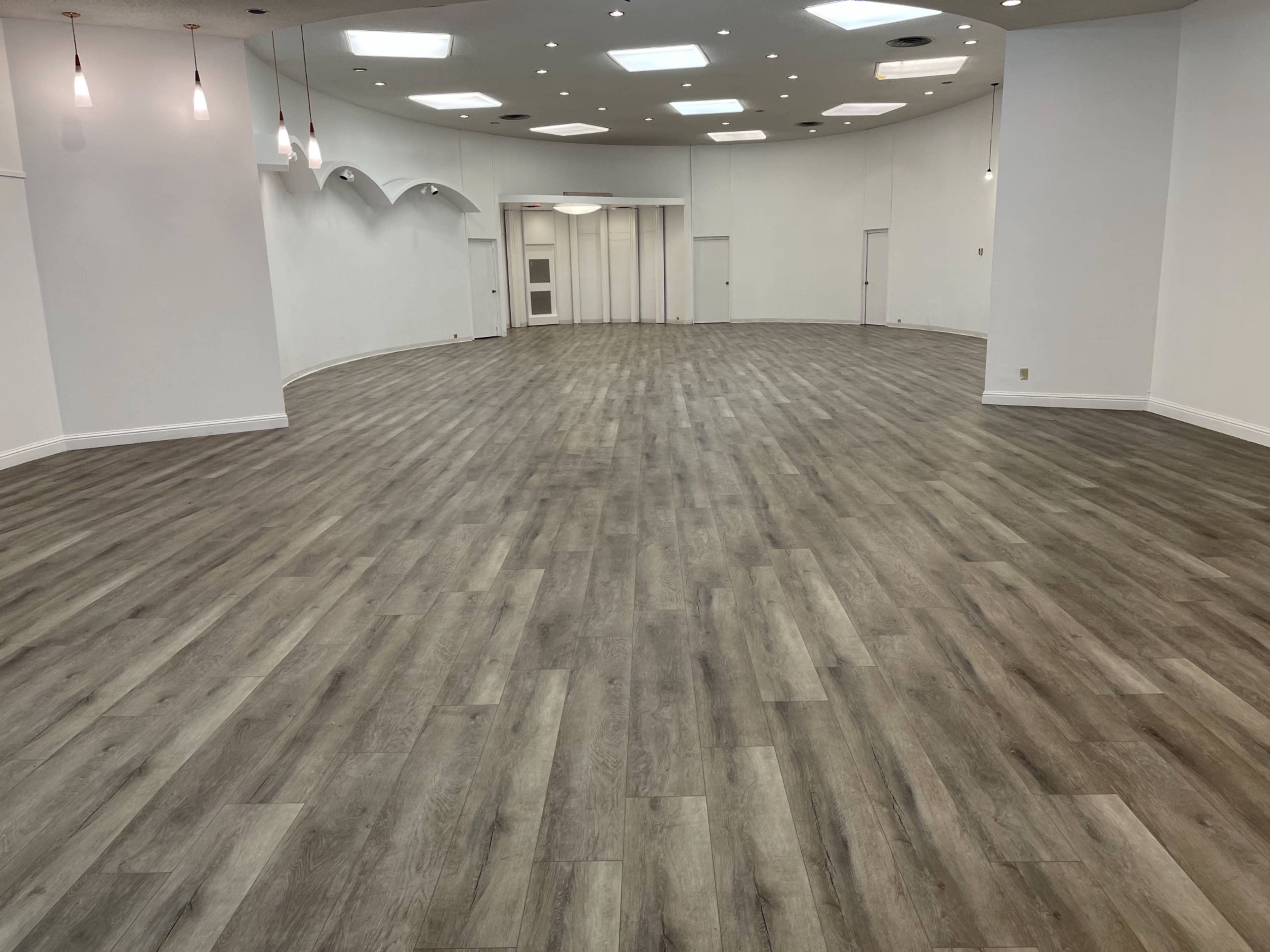 A large, empty room with a wooden floor and a curved, white wall featuring recessed areas and ceiling lights.