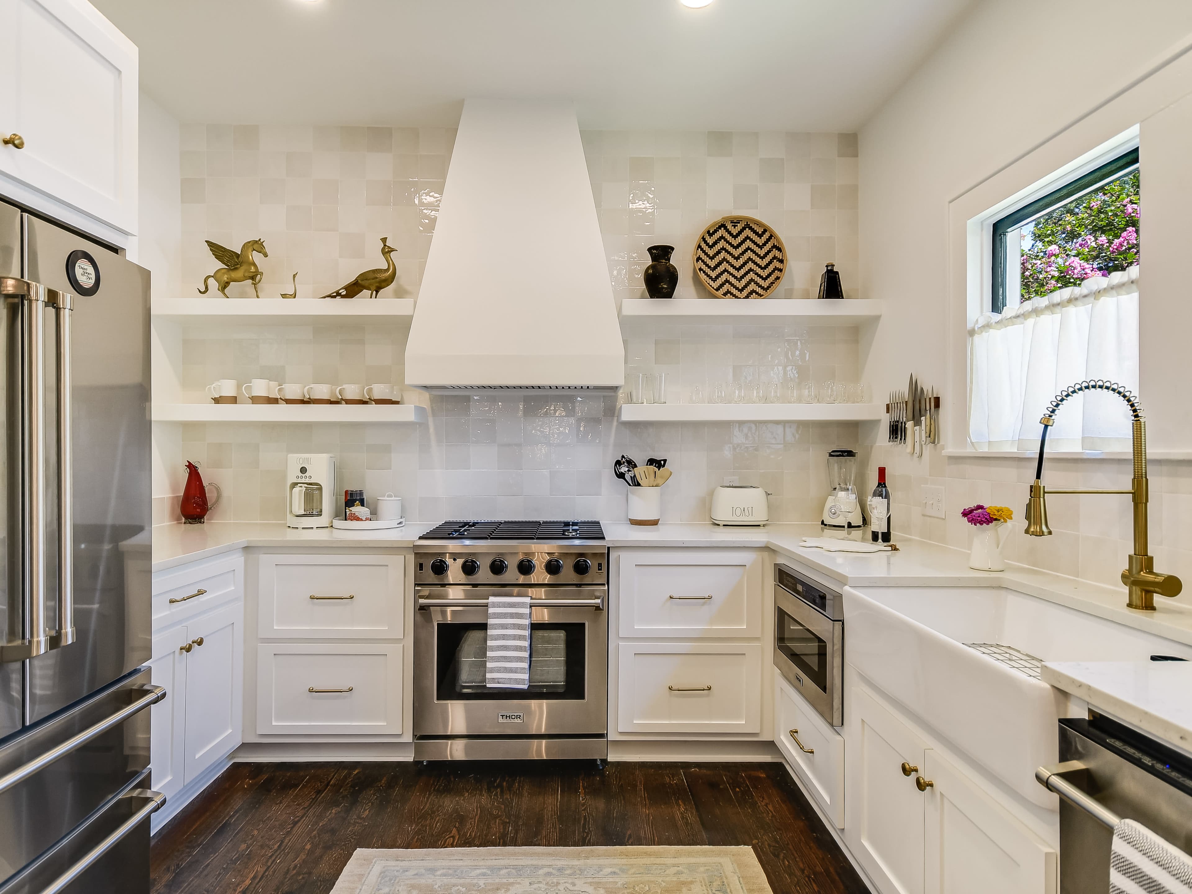 A modern kitchen with white cabinetry, stainless steel appliances, and open shelves displaying decorative items.