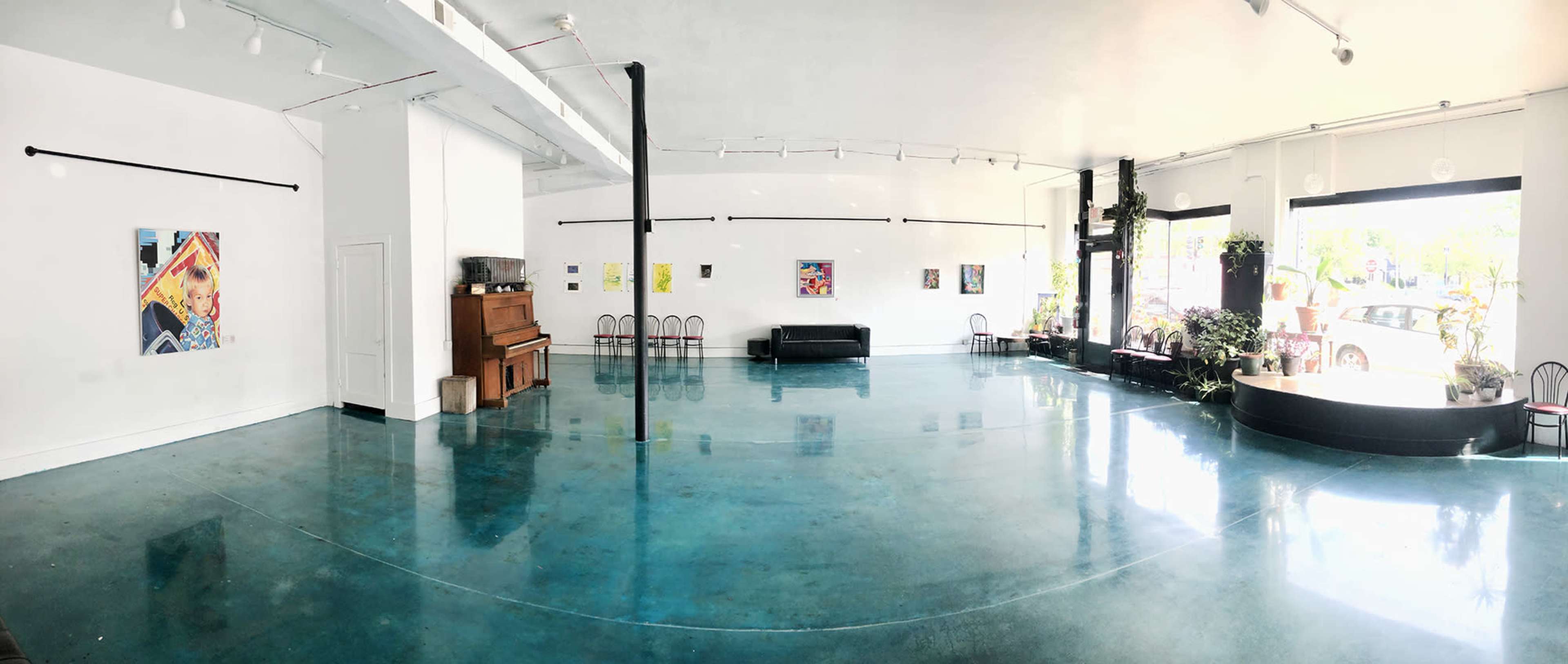 The image shows a spacious art gallery with polished turquoise flooring, featuring a piano and several artworks displayed on the white walls.