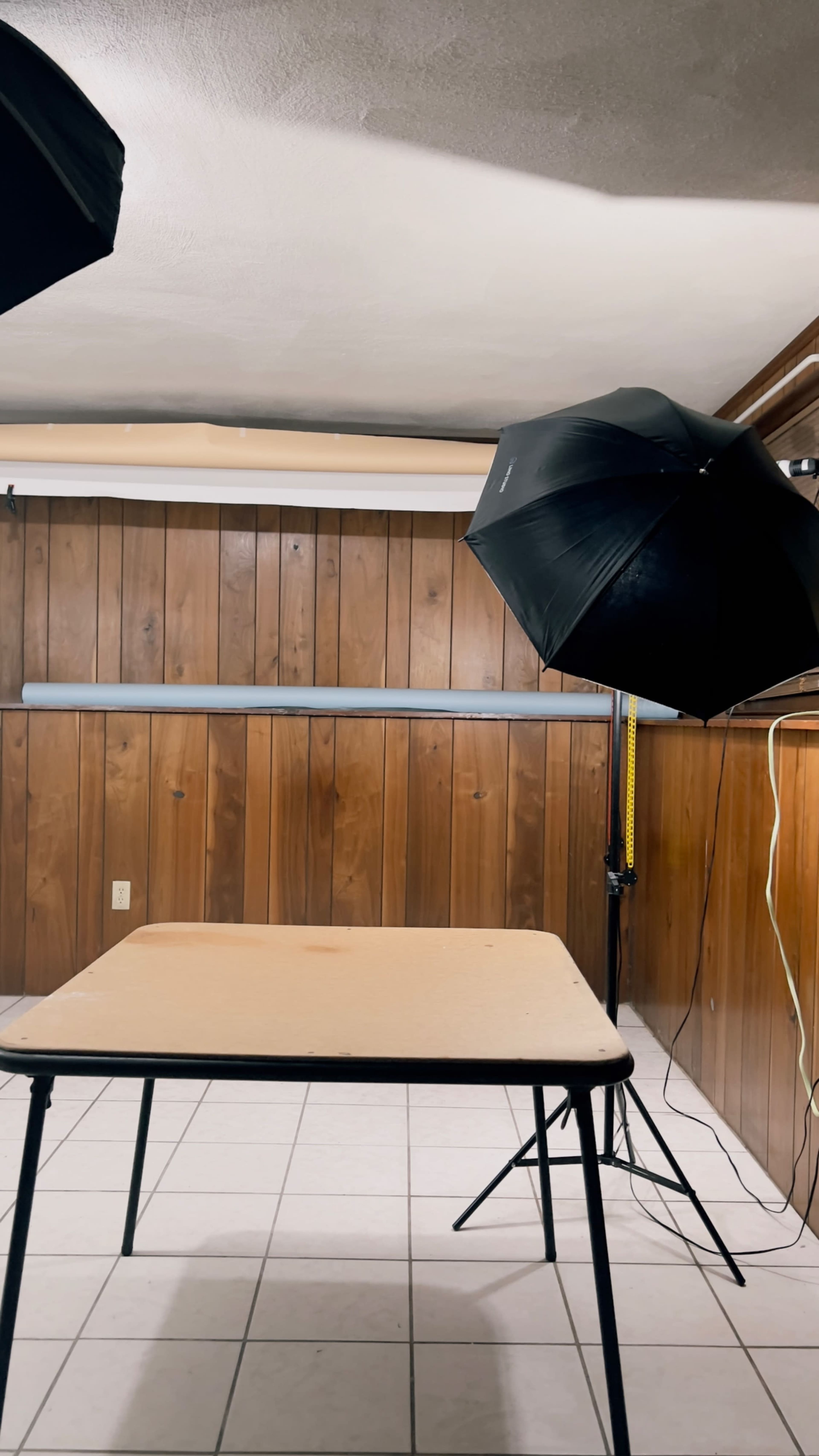 A simple photography setup with a table under soft lighting from an umbrella reflector in a room with wooden paneling.