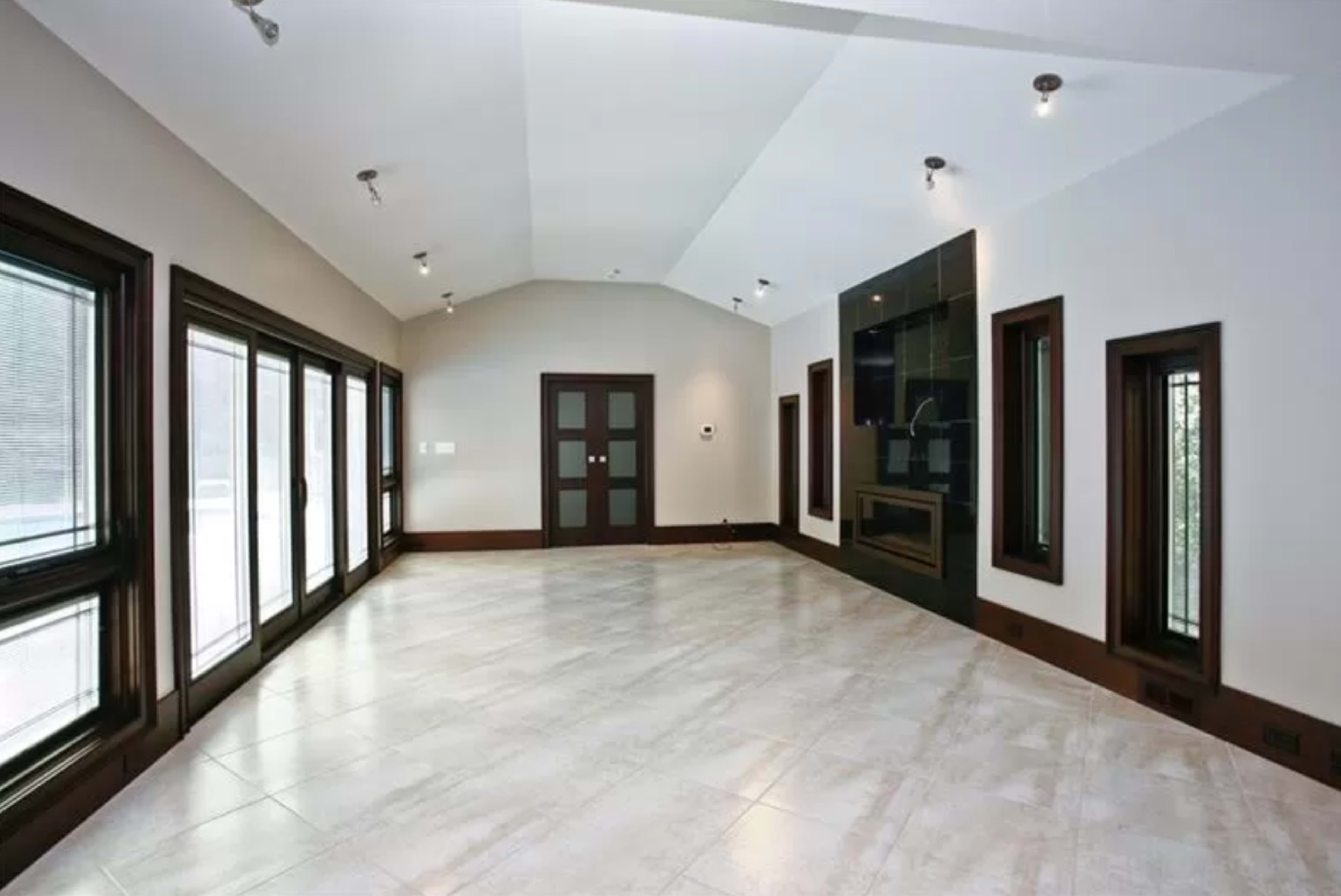 A spacious, empty room with a high ceiling, large windows, and modern light fixtures.