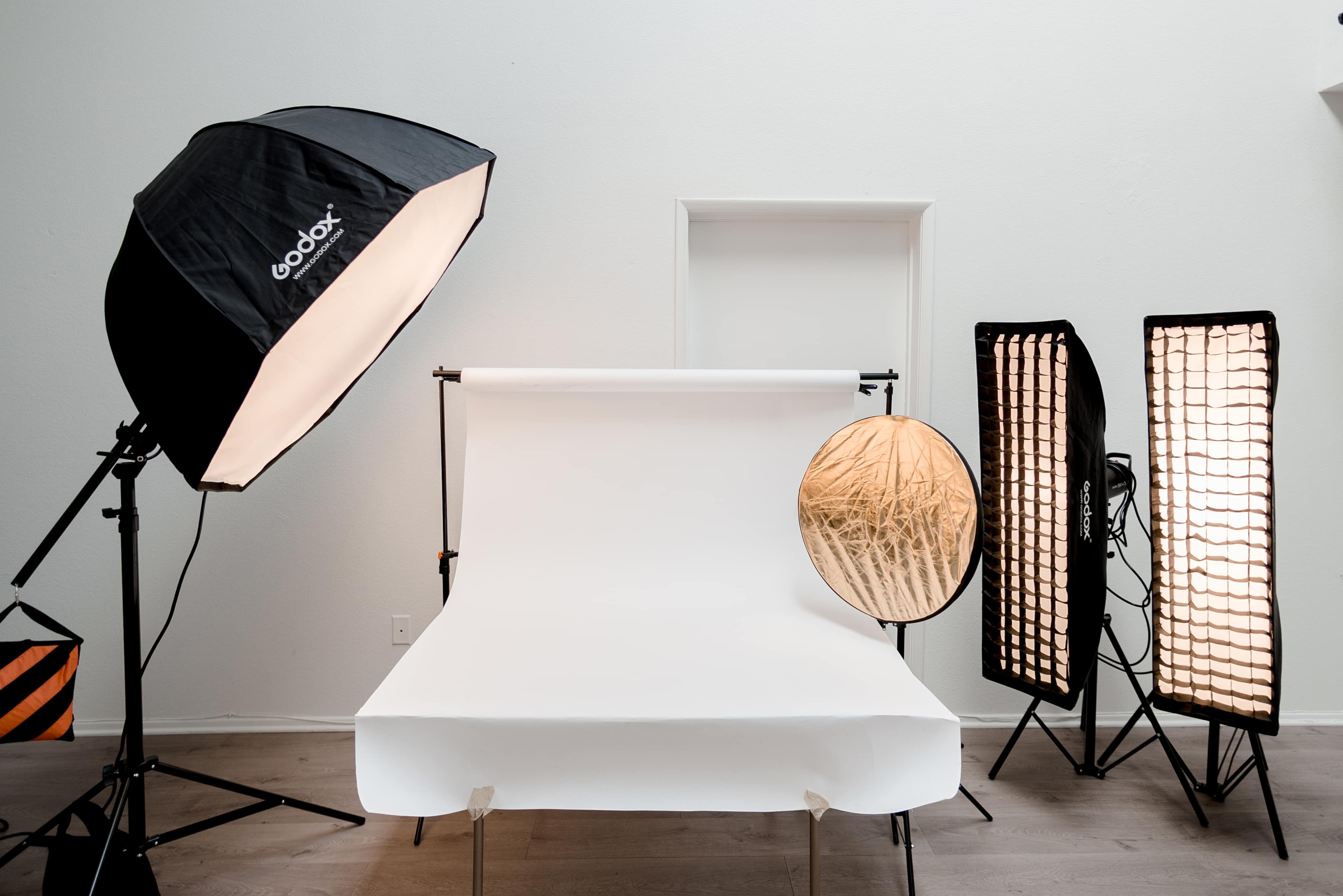 A photography studio setup featuring a white backdrop, softbox lighting, and a round reflector.