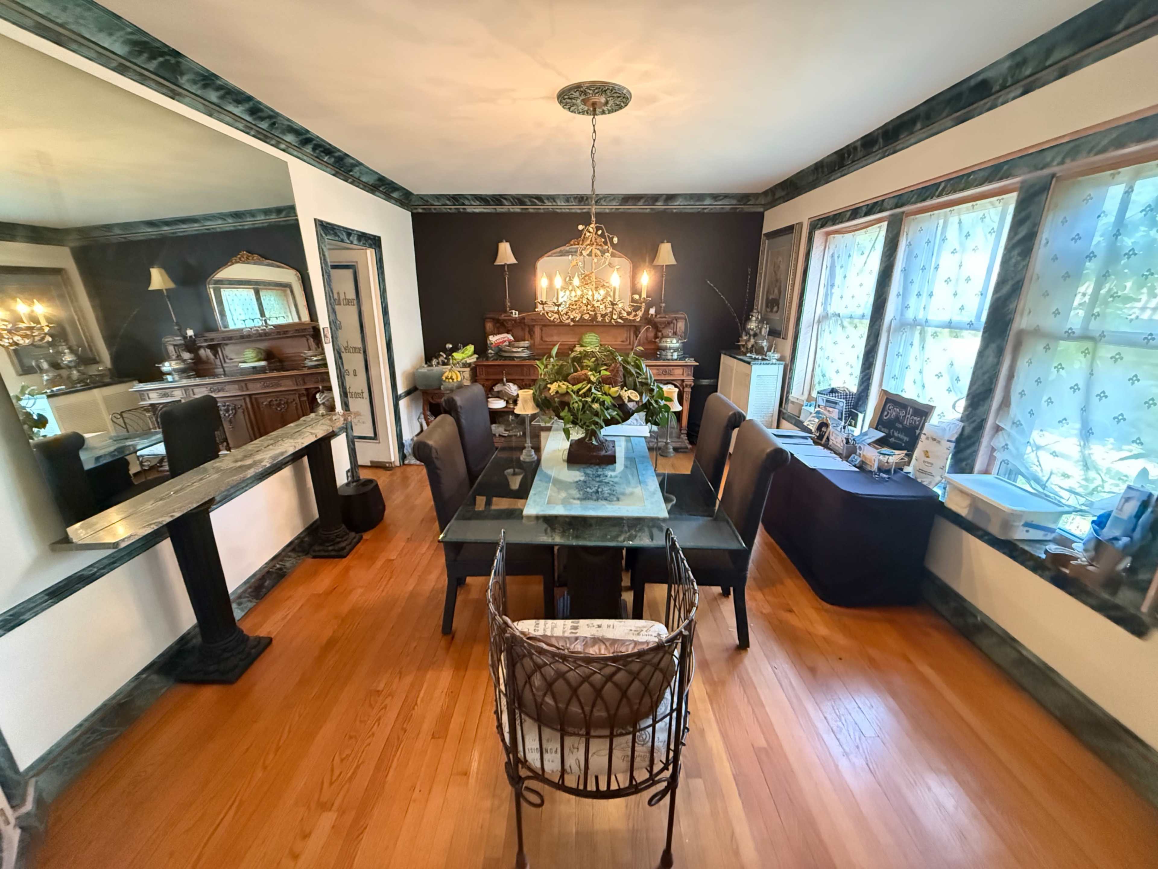 The dining room features a central glass table surrounded by chairs, with a chandelier overhead and mirrored walls reflecting the decor.