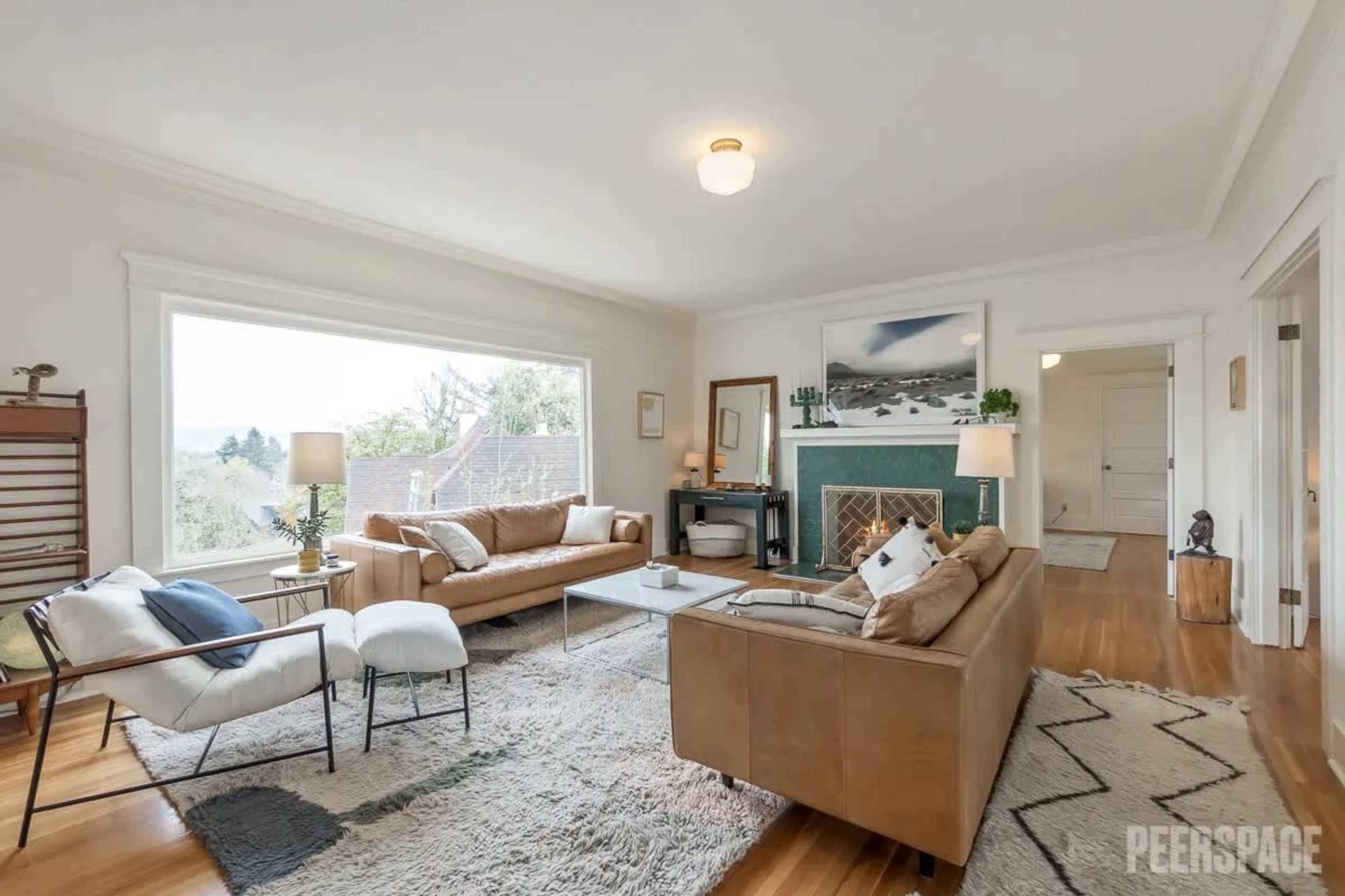 The living room features two sofas, a coffee table, and a large window providing natural light, with a fireplace and artwork on the walls.