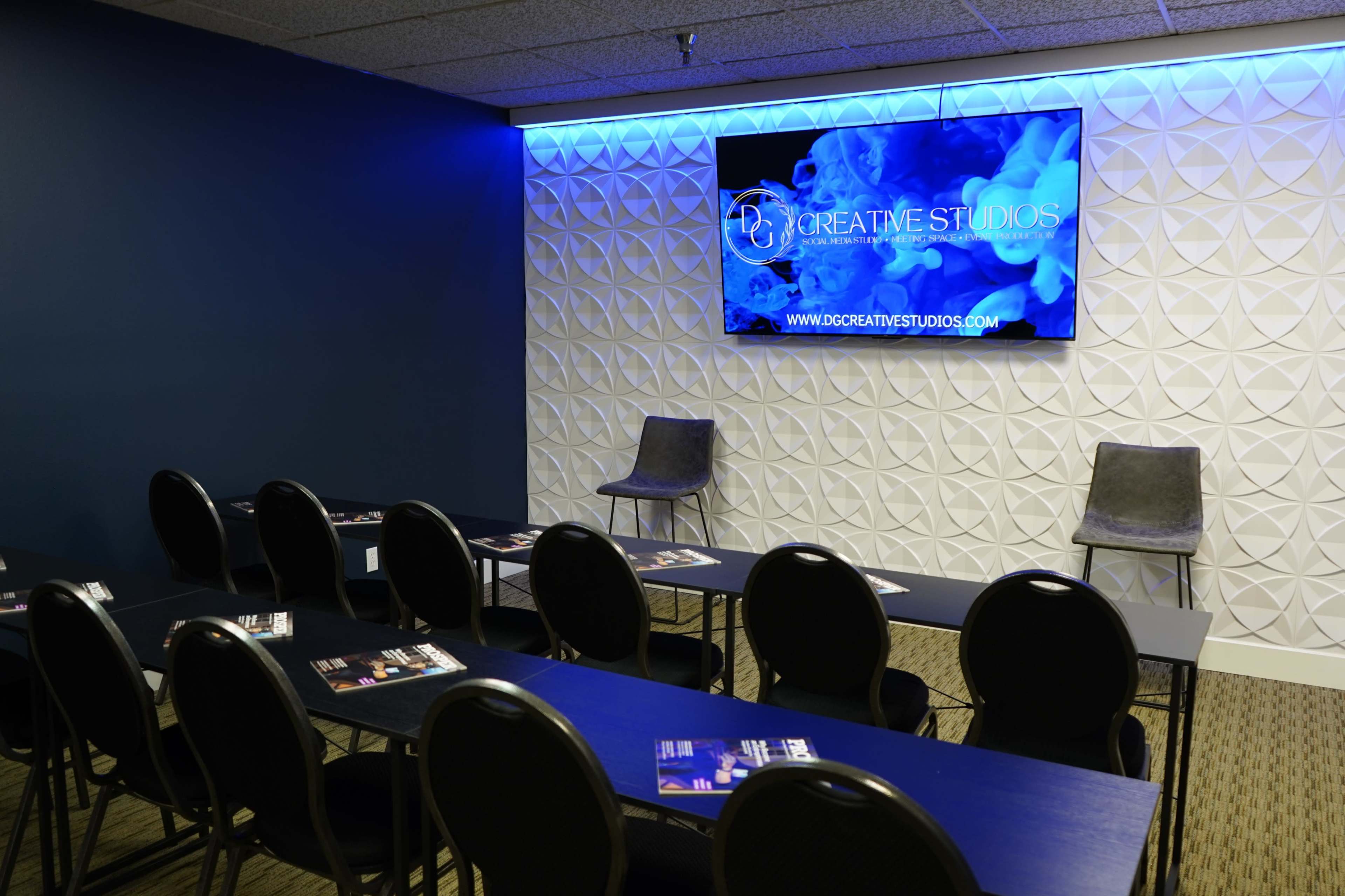 A conference room with rows of black tables and chairs facing a large screen displaying the logo of Creative Studios.