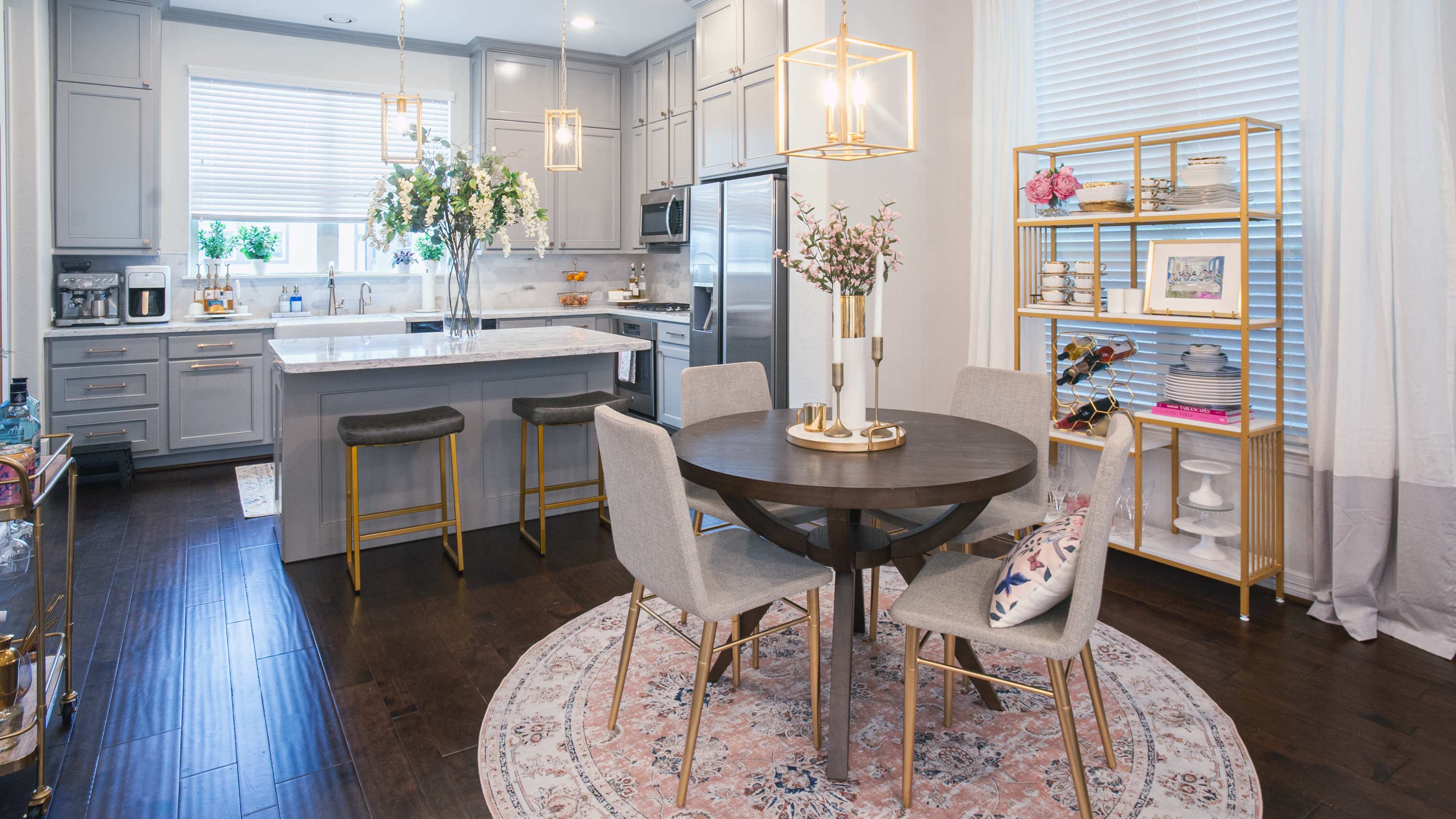 A modern kitchen and dining area with gray cabinetry, a round wooden table surrounded by four chairs, and a decorative gold shelving unit.