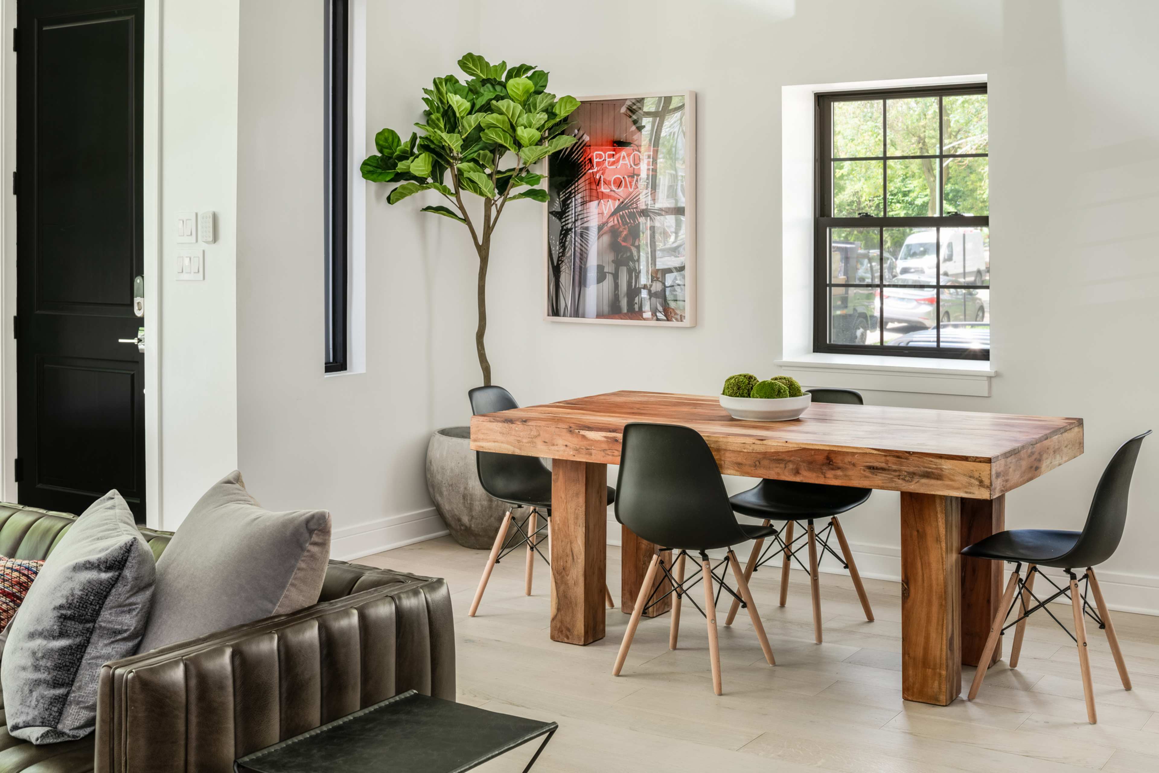 A wooden dining table surrounded by black chairs is positioned near a window and a decorative plant in a modern interior.