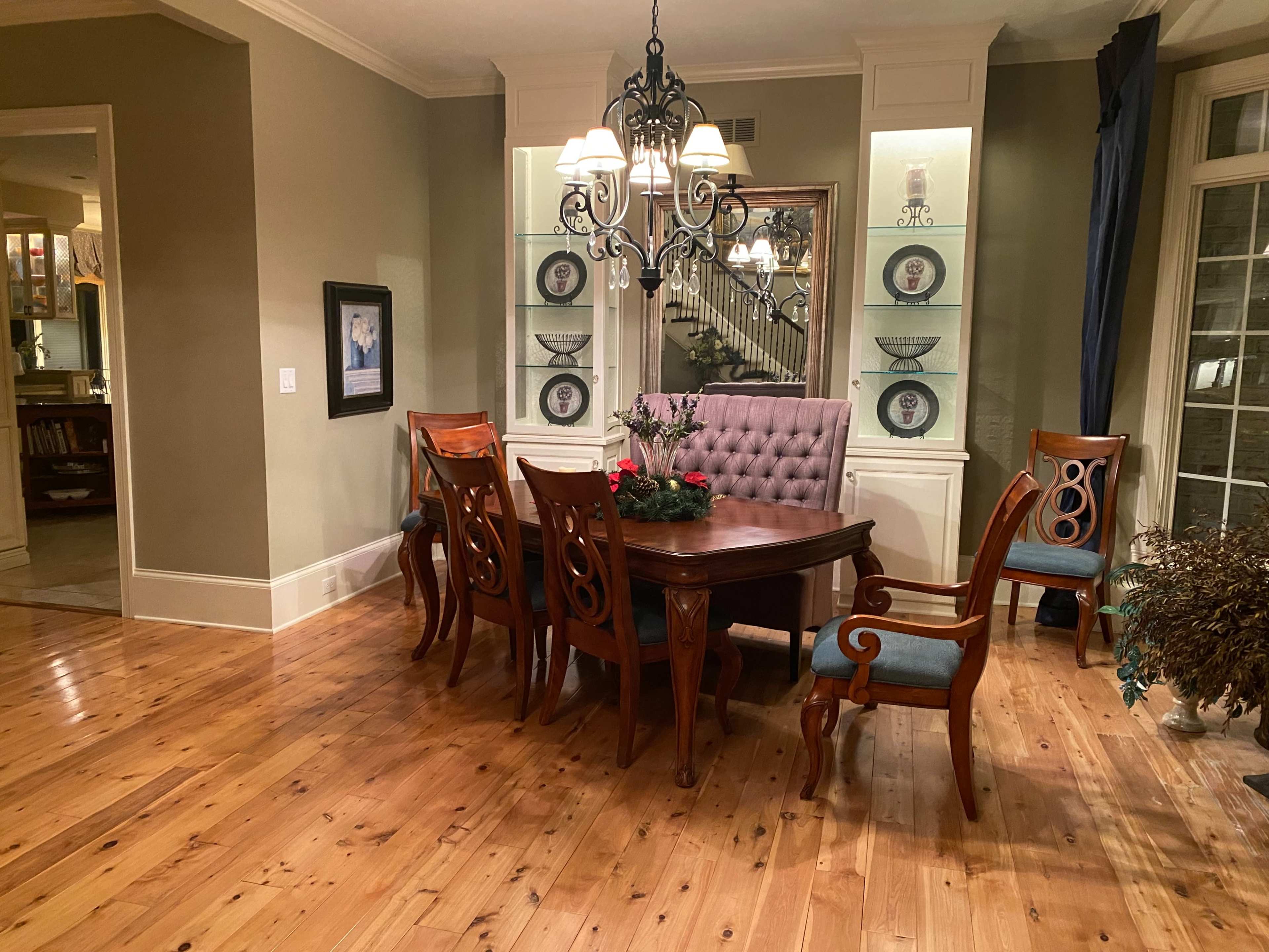 A dining room with a wooden table surrounded by four chairs and a tufted backrest chair, illuminated by a chandelier and accented by decorative wall displays.