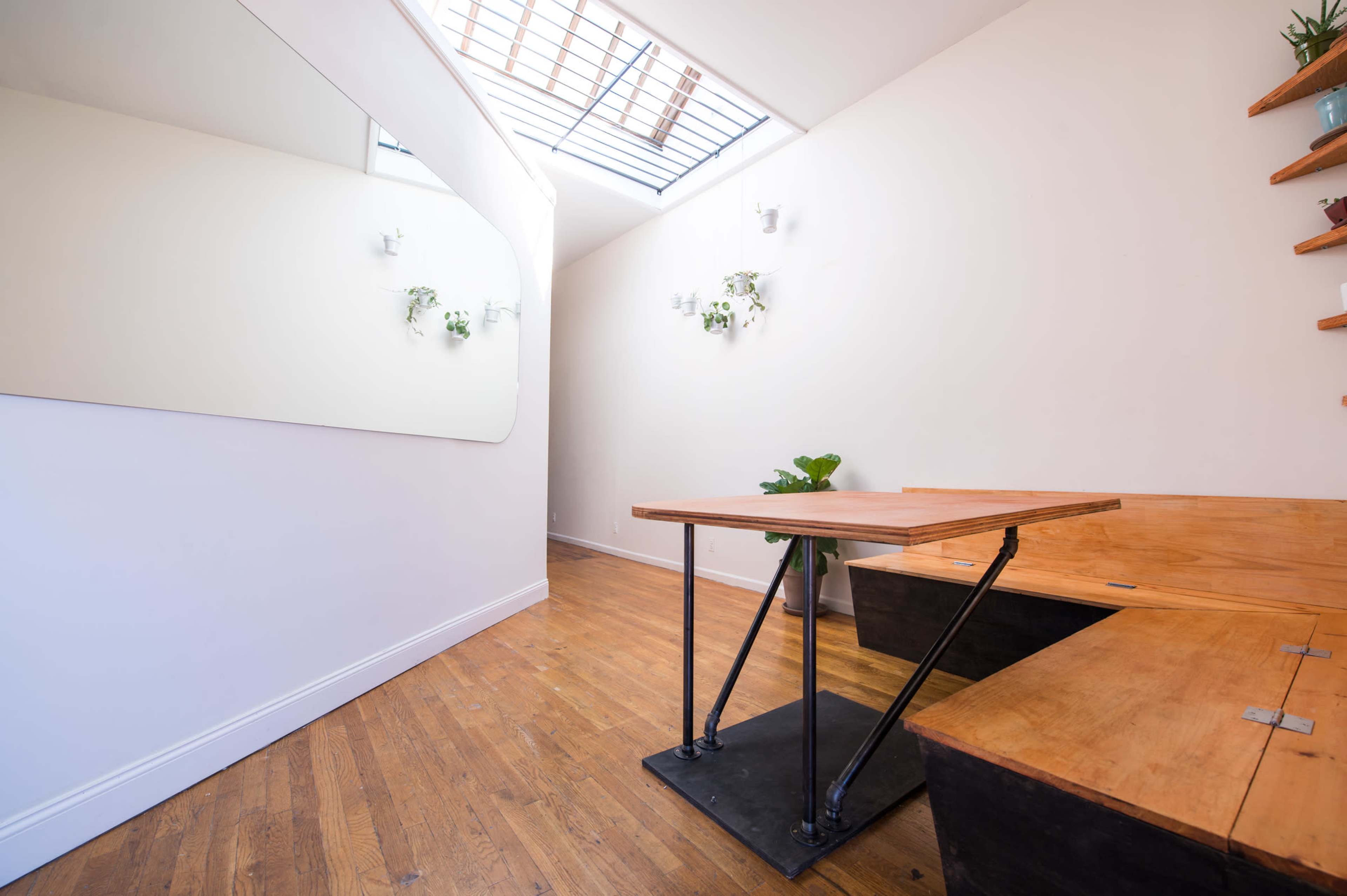 A minimalist interior space featuring a wooden table, benches, and a skylight with plants on the walls.