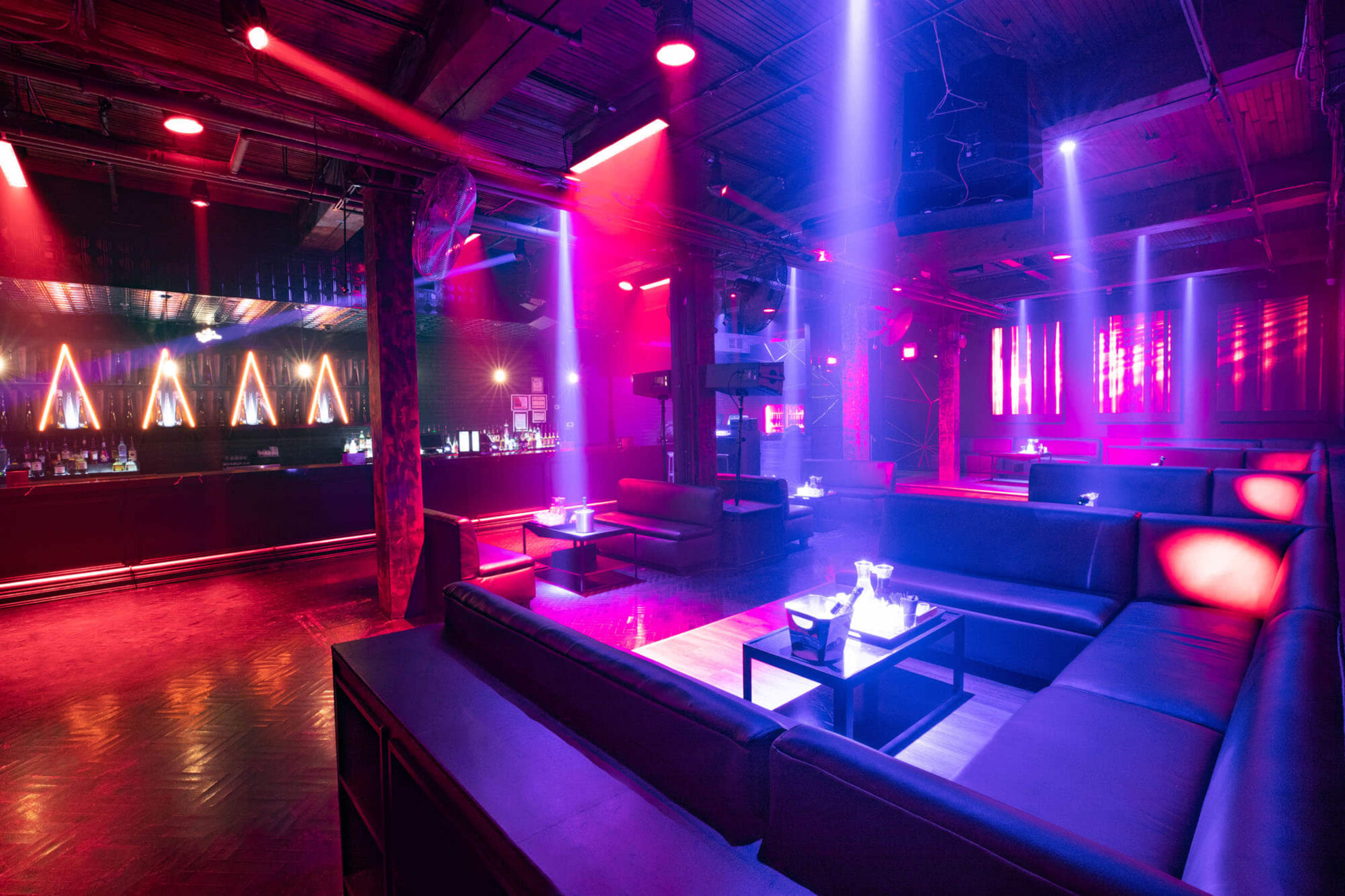 The image shows a modern nightclub interior with leather seating, dim lighting, and colorful laser lights illuminating the space.