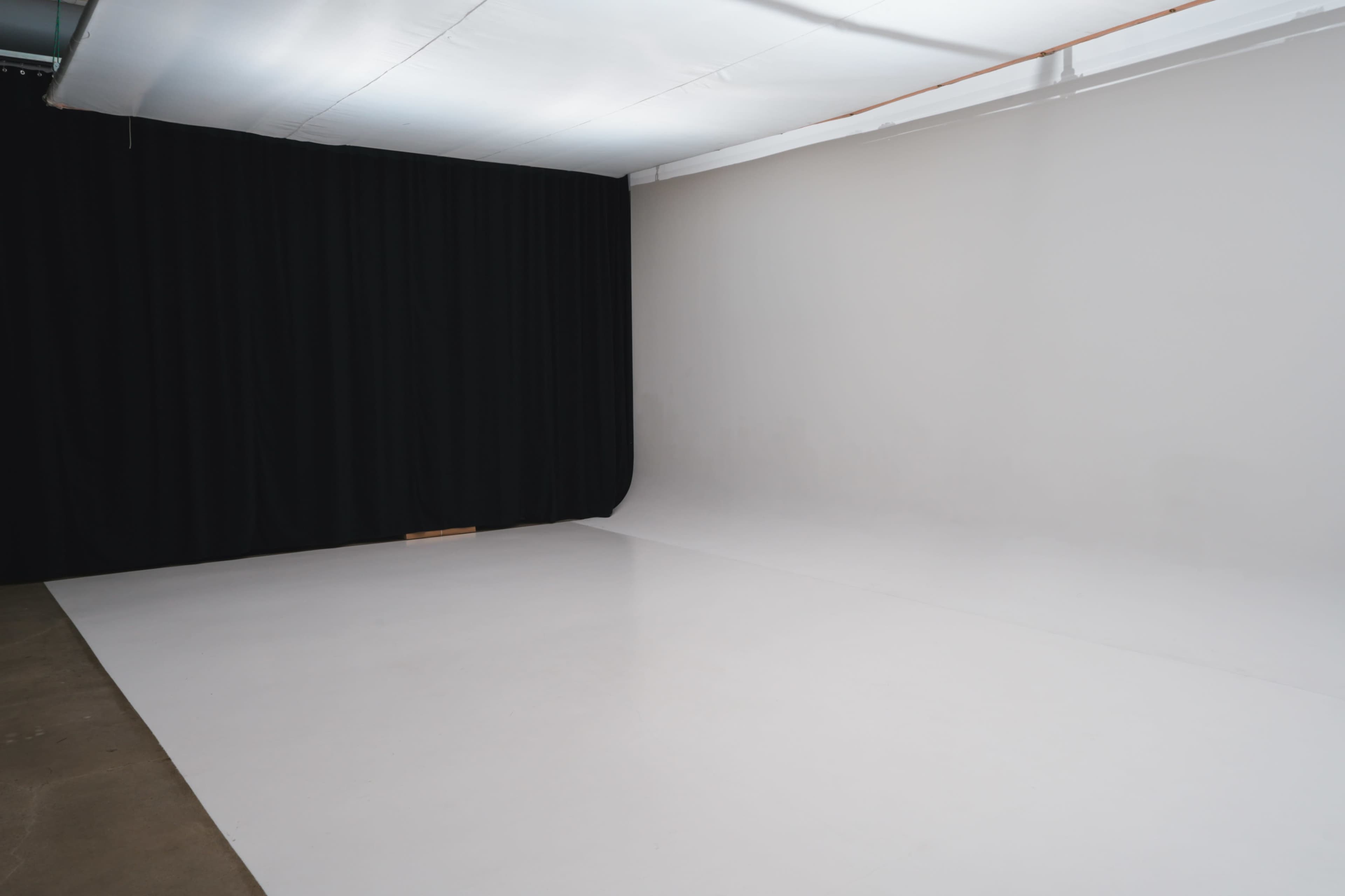 The image shows a spacious studio with a white floor and a backdrop of black curtains on one side.