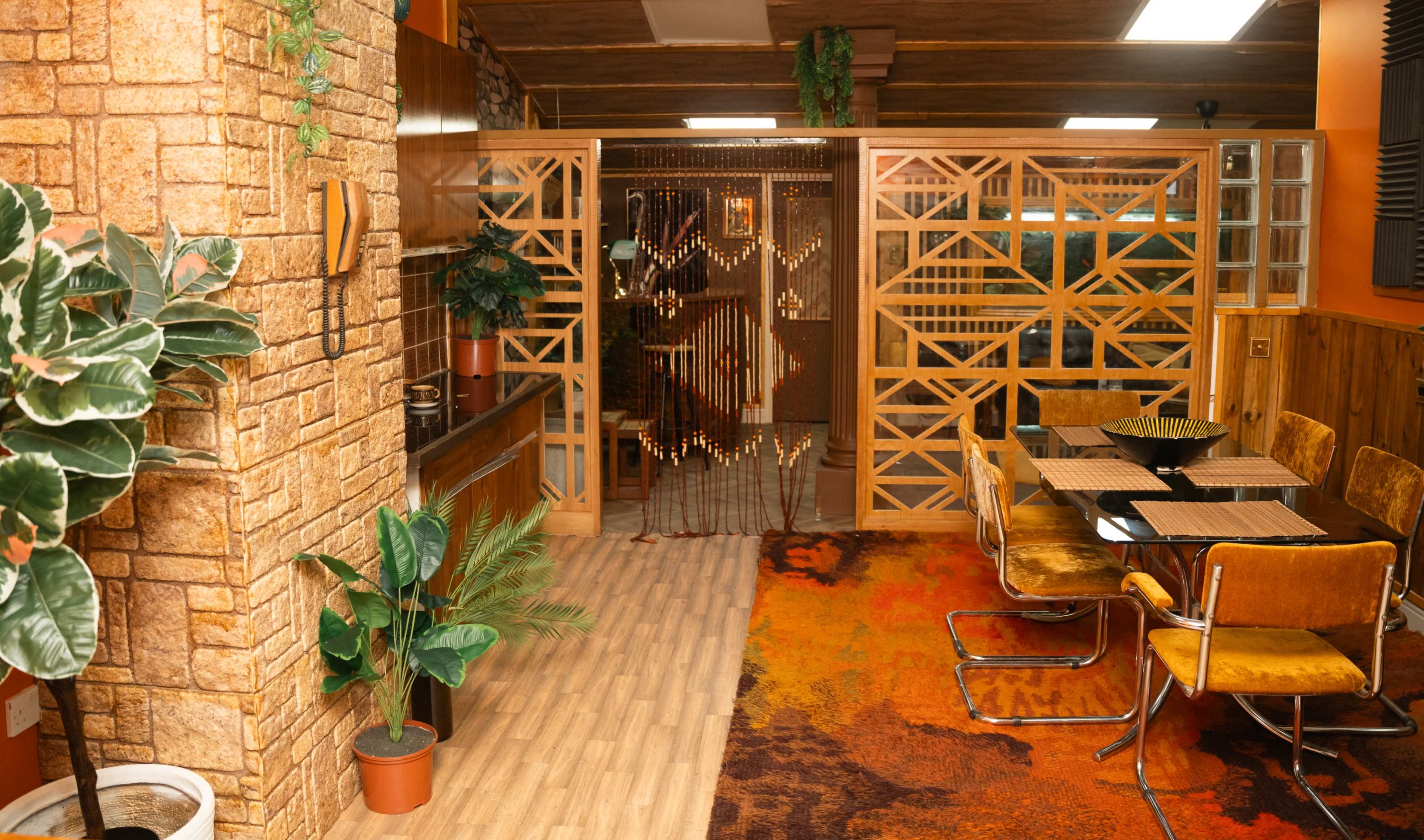 A cozy interior space featuring wooden paneling, a patterned rug, and a dining area with yellow chairs beside a wooden table.