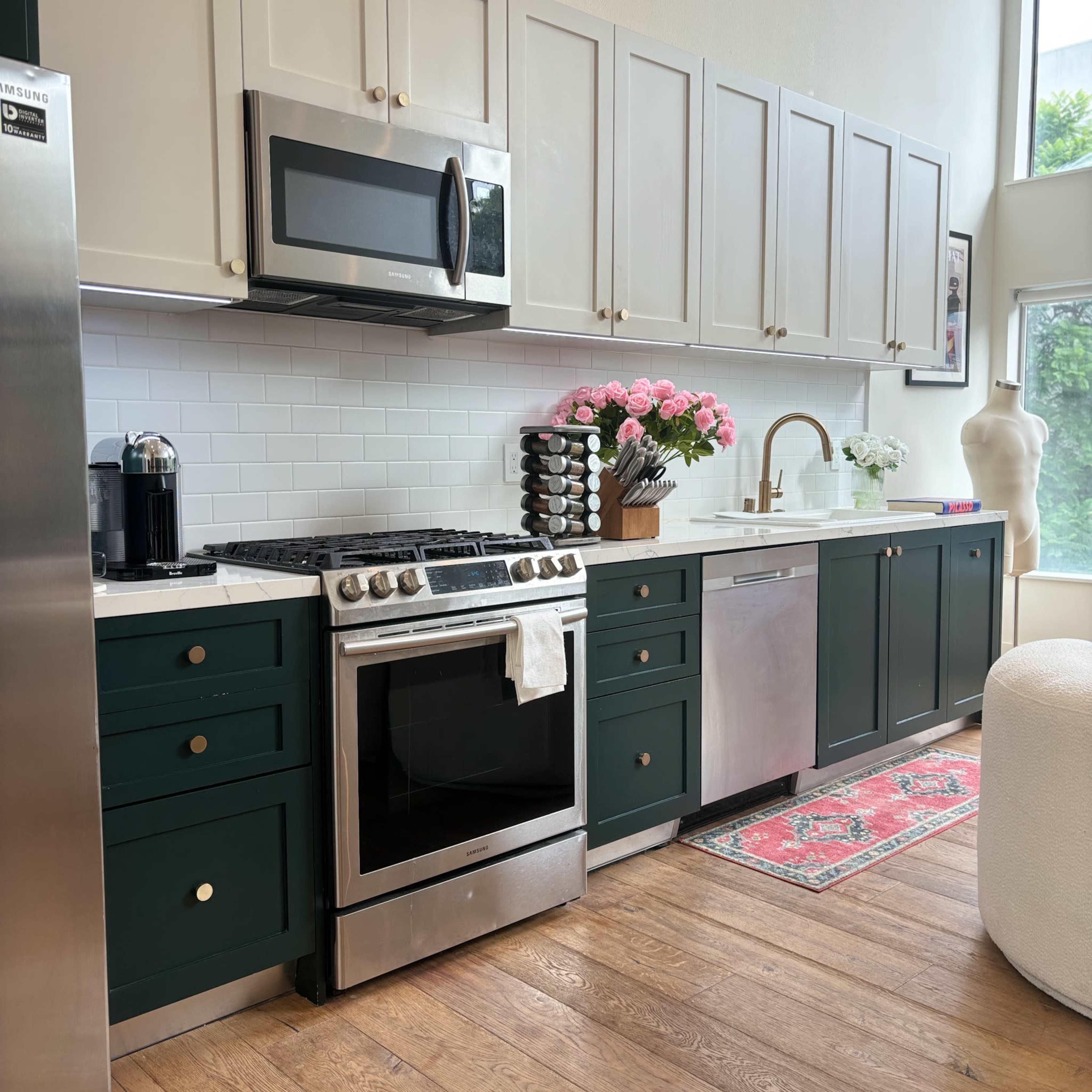 A modern kitchen features green lower cabinets, stainless steel appliances, and decorative pink flowers on the countertop.