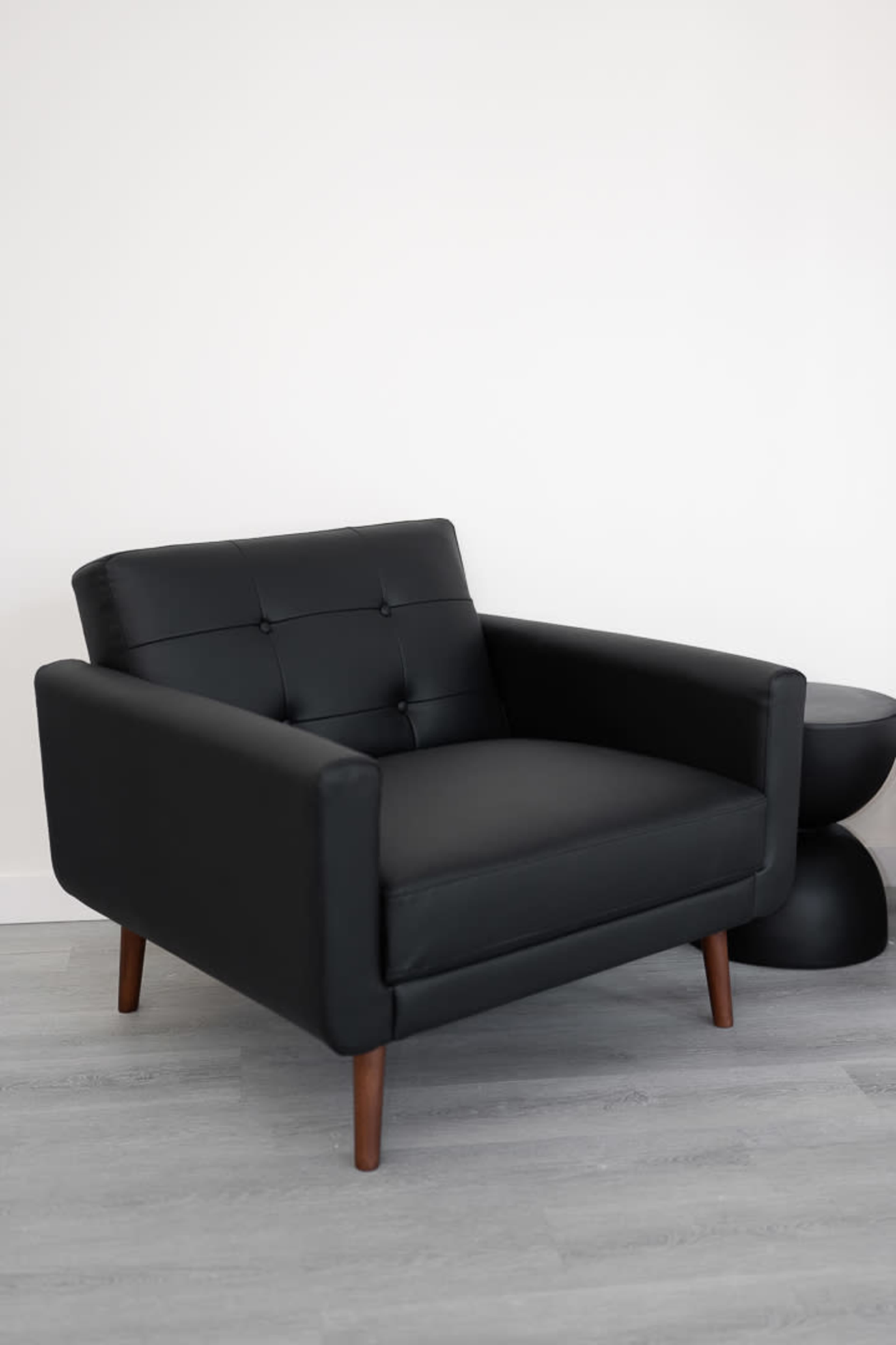 The image shows a modern black armchair with wooden legs placed next to a round black side table.