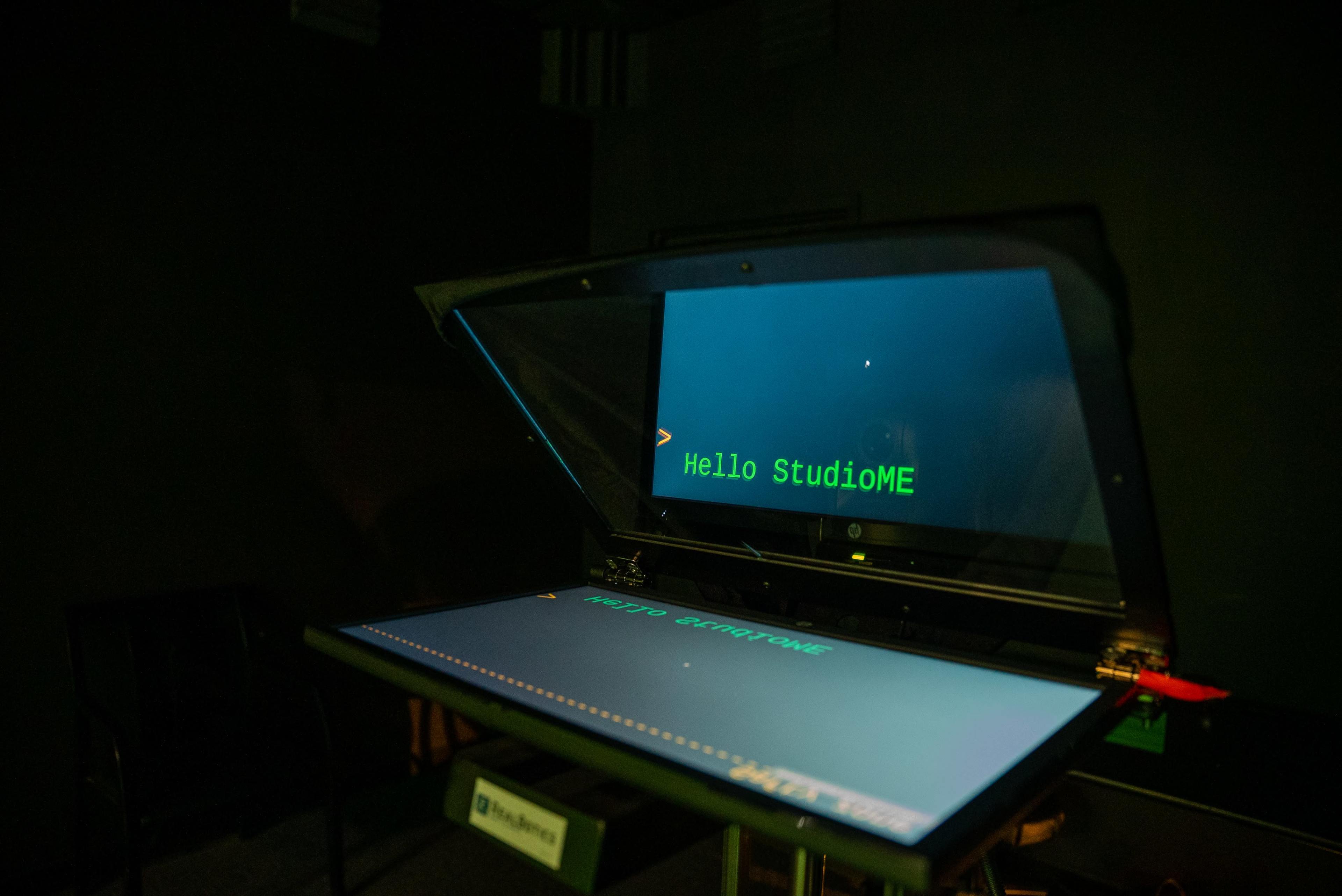 A digital display with a translucent screen shows the text "Hello StudioME" in a dimly lit room.